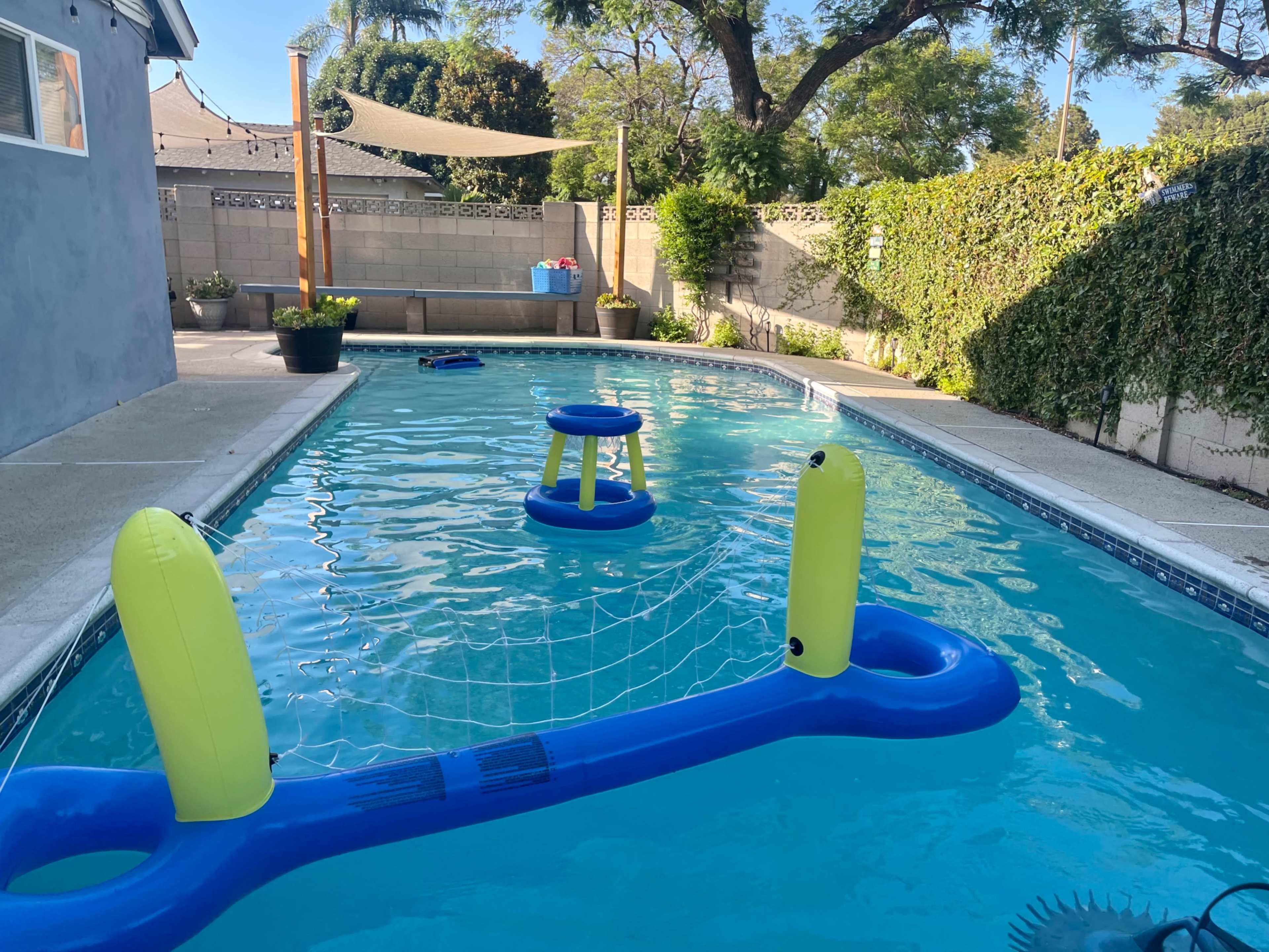 A swimming pool with a floating volleyball net and two inflatable chairs on the water.