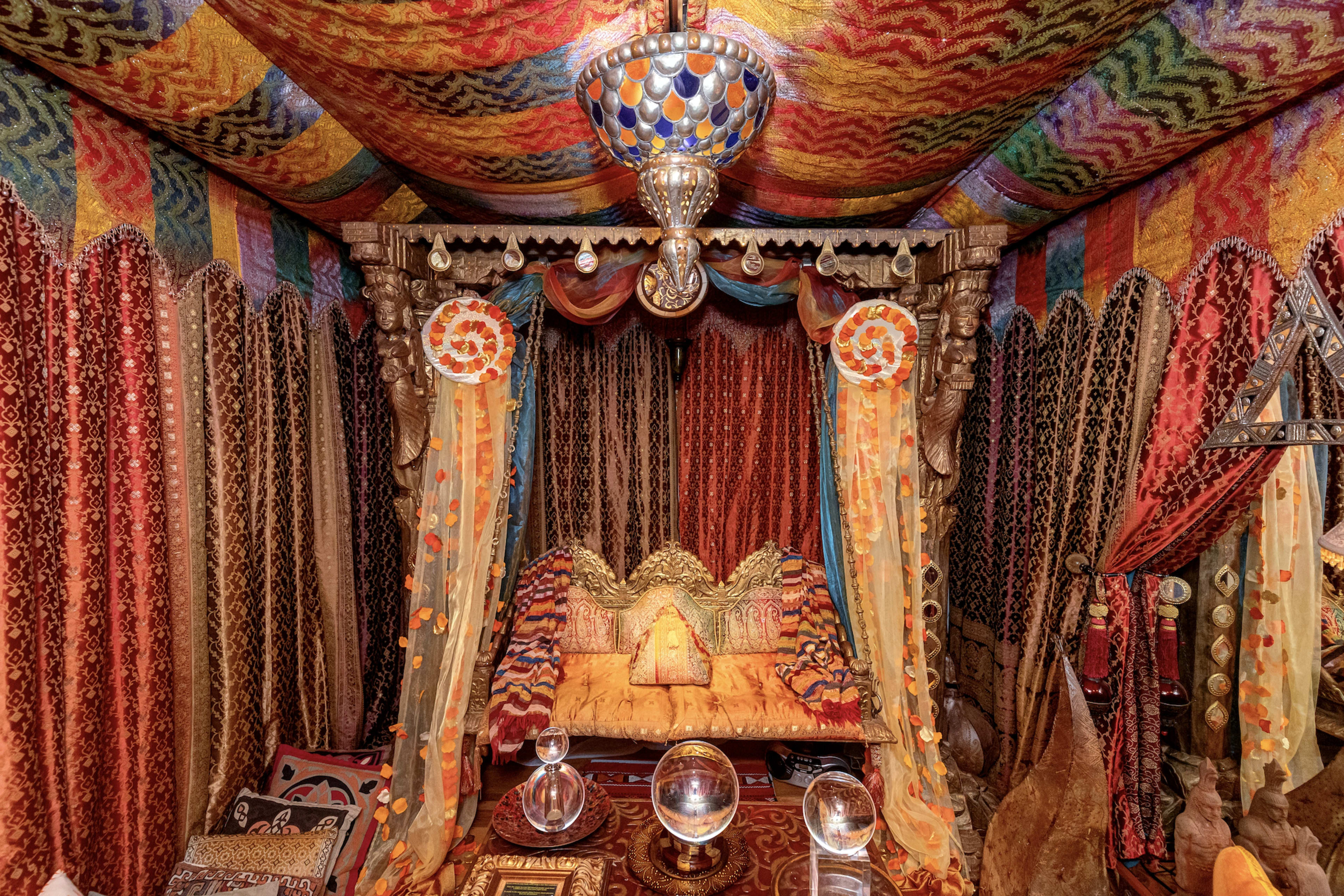 A richly decorated interior space resembling a Moroccan-style lounge, featuring vibrant fabrics, a decorative ceiling, and ornate seating.