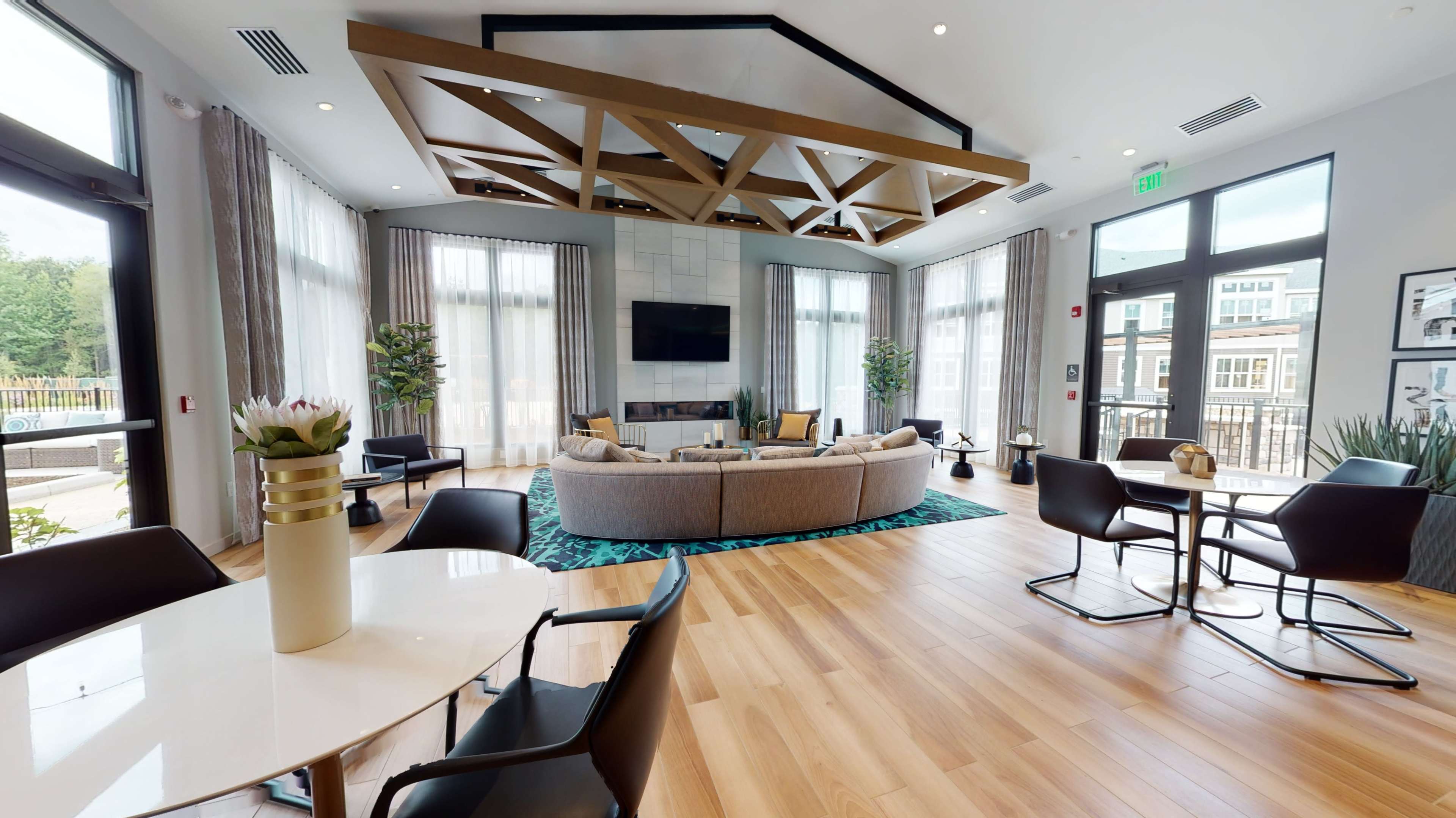 A modern common area with a large circular sofa, a wooden ceiling structure, and large windows allowing natural light to fill the space.