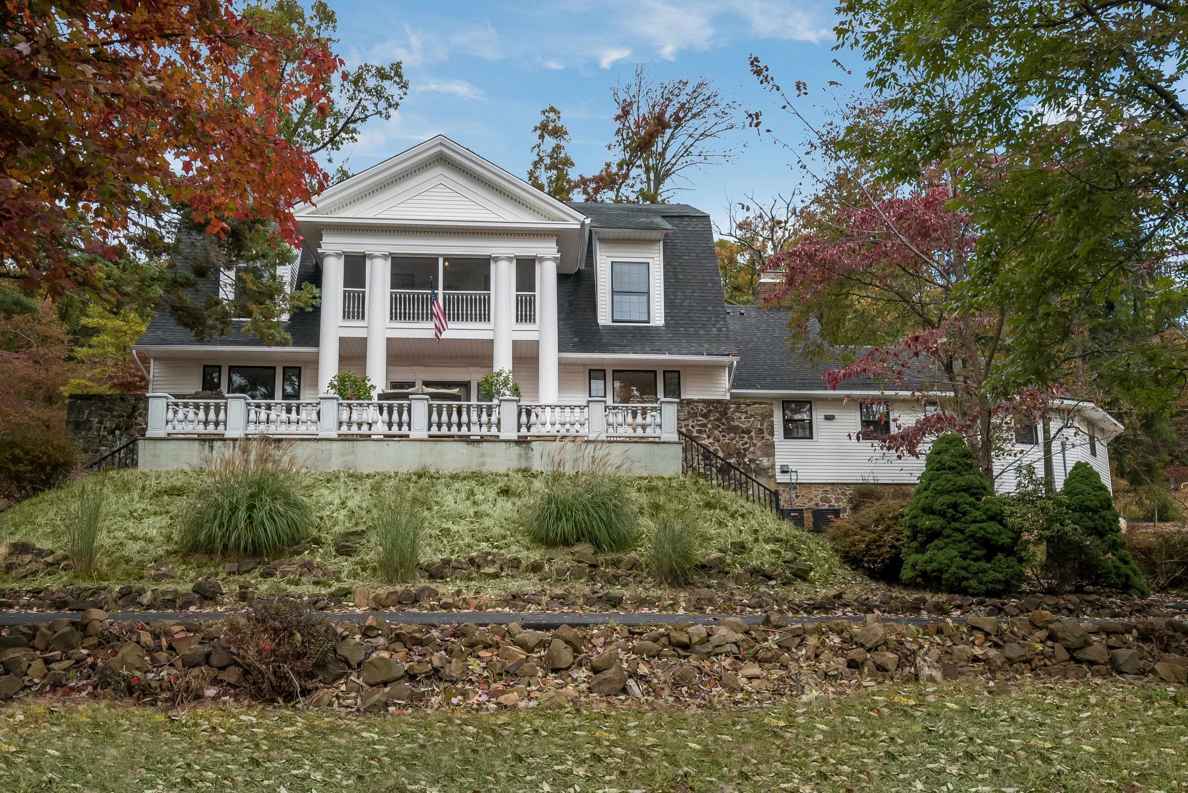 A two-story house with a front porch, surrounded by trees and landscaped grounds, is located on a grassy hillside.