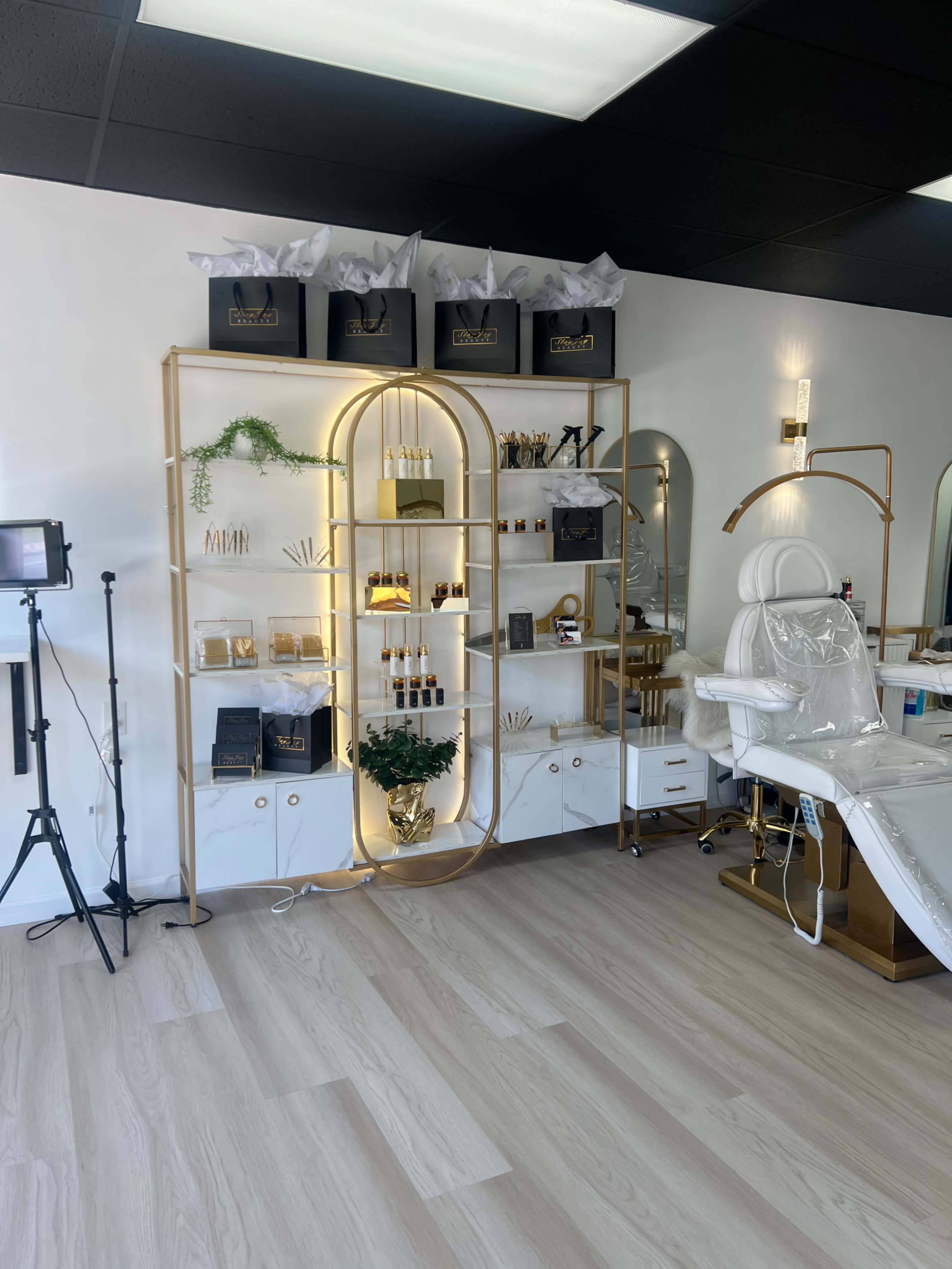 A well-organized beauty salon interior featuring a display shelf with various cosmetics and tools, a treatment chair, and a professional lighting setup.