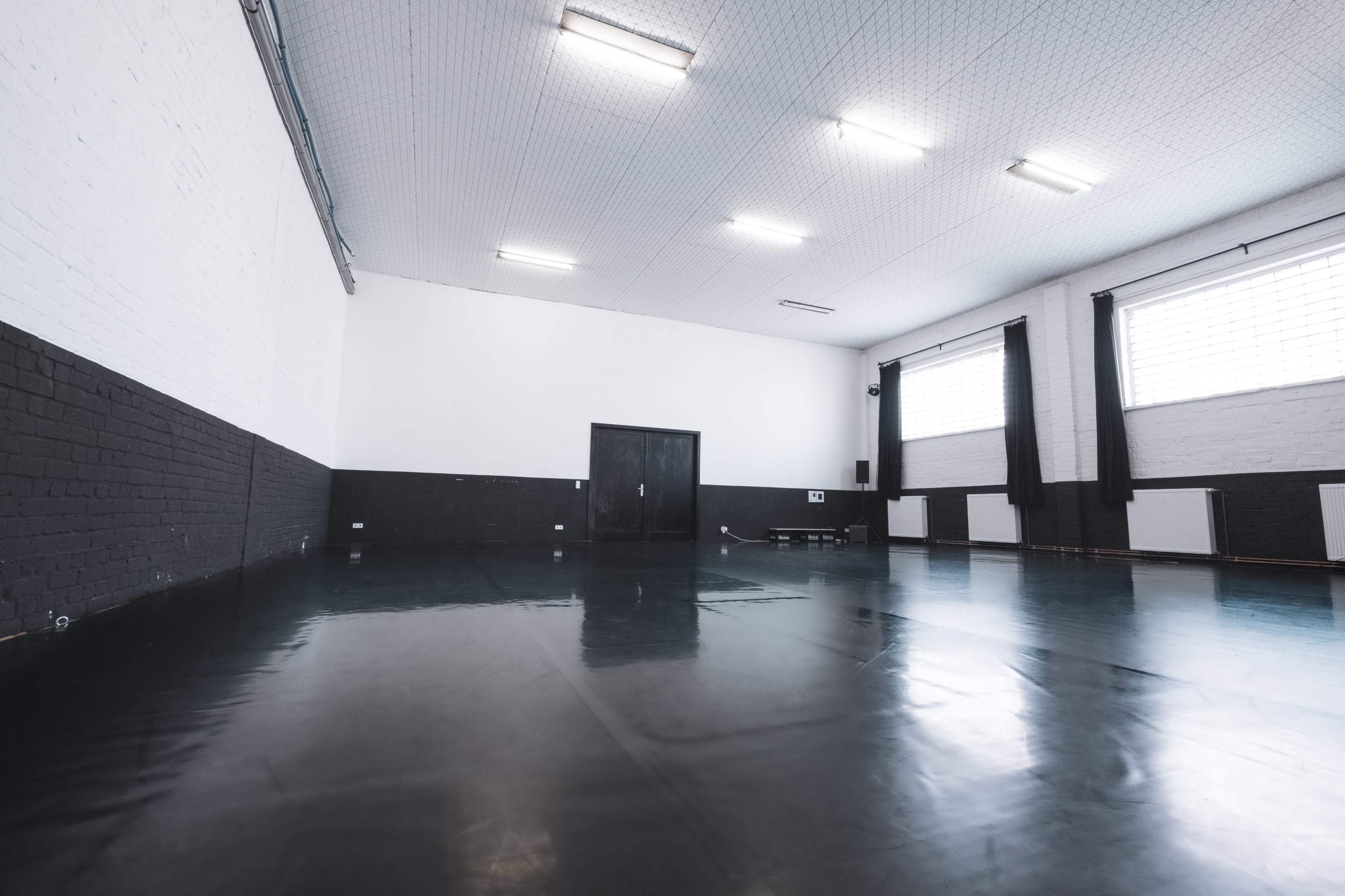 A spacious indoor room with black and white walls, fluorescent lighting, and a shiny floor.