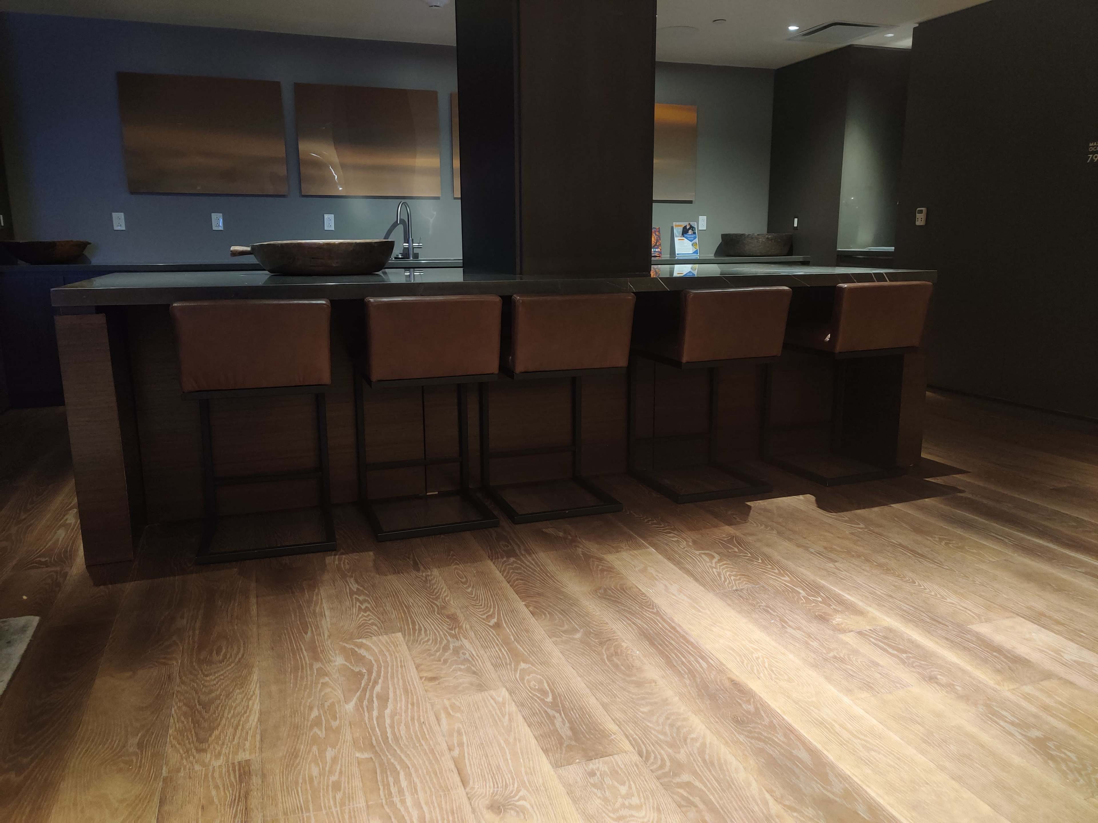 A modern kitchen island with four brown leather bar stools and wooden flooring.