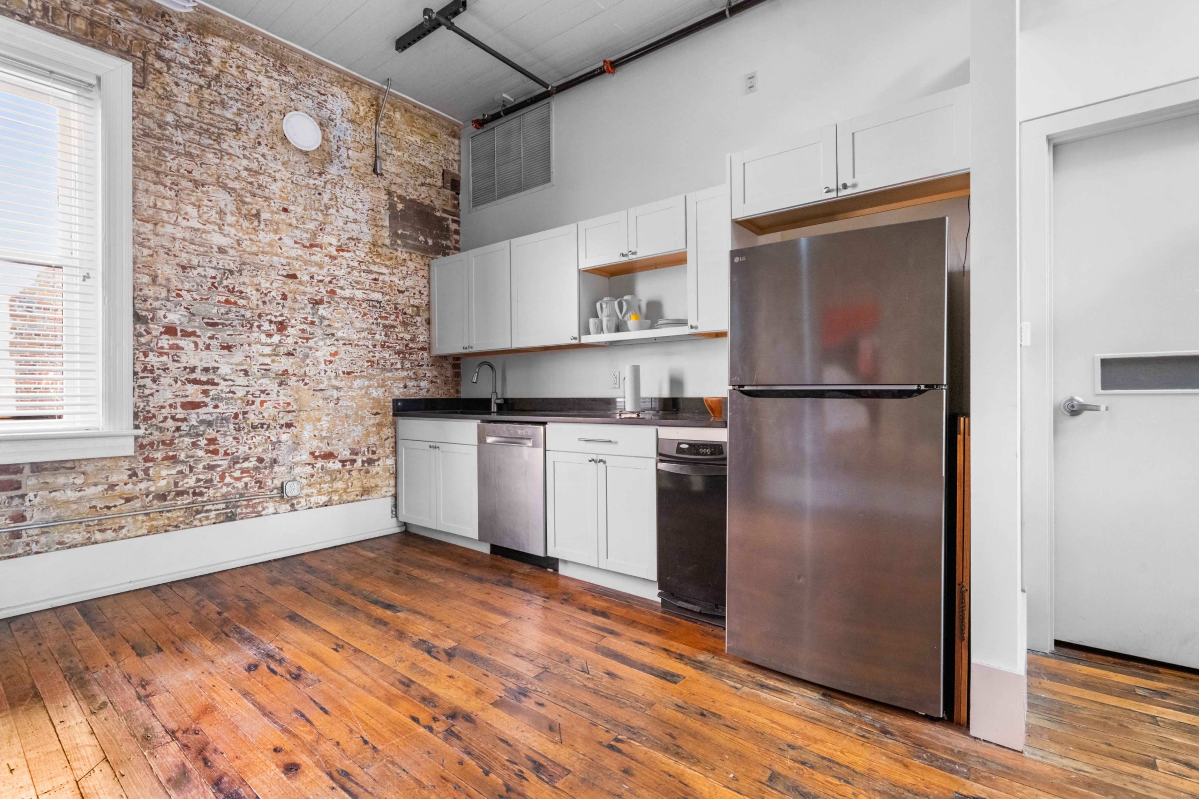 The image shows a kitchen with exposed brick walls, wooden flooring, and modern appliances, including a refrigerator and dishwasher.