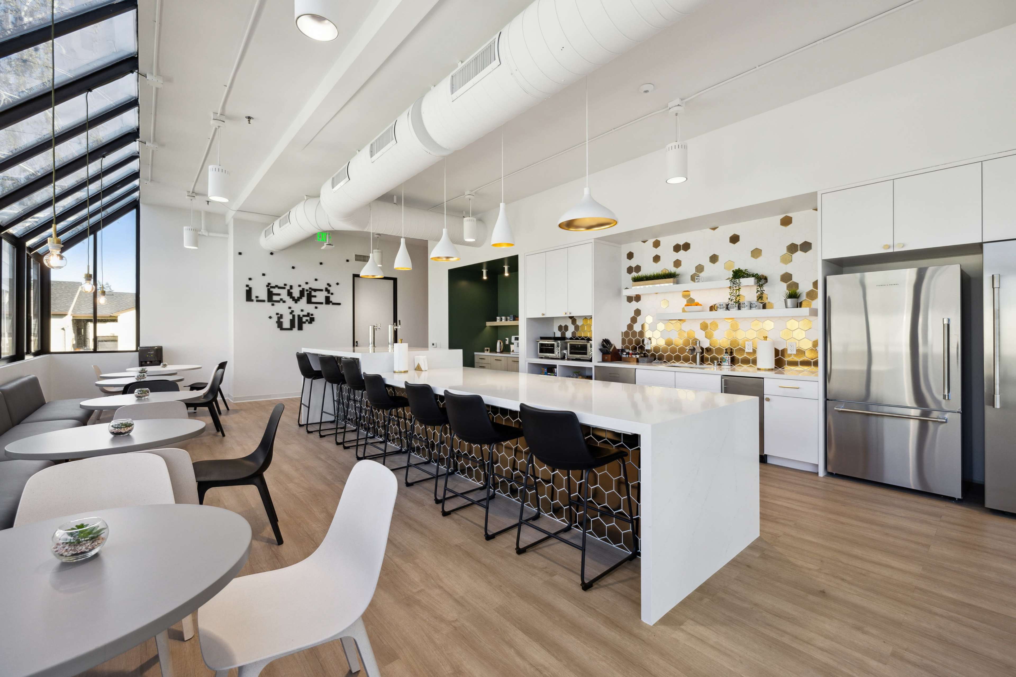 The image shows a modern kitchen and dining area featuring a large island with bar seating, white cabinetry, and decorative wall elements.