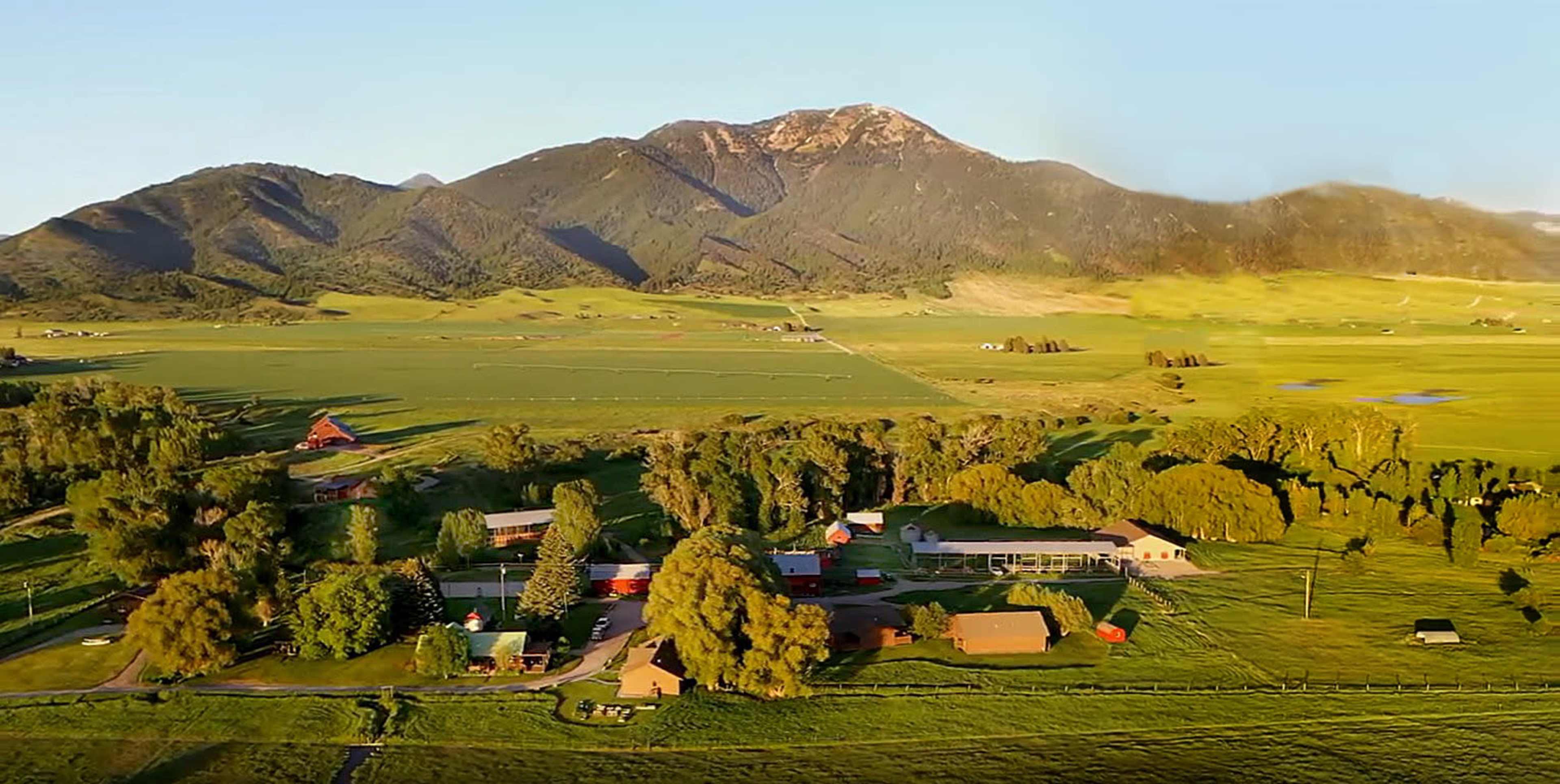 A rural landscape featuring a collection of buildings and fields set against a backdrop of mountains.