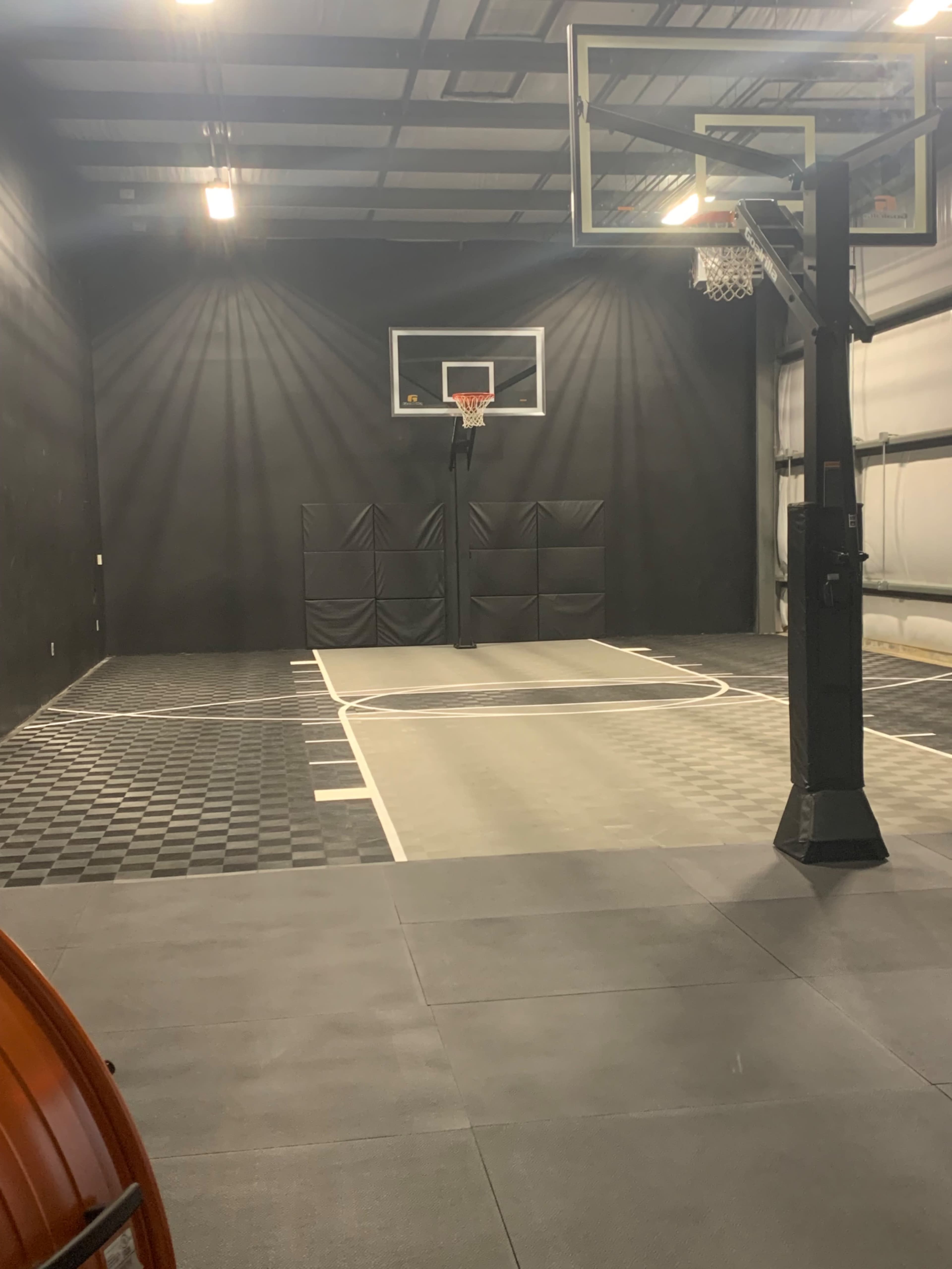 An indoor basketball court with a black wall, a basketball hoop, and a multi-colored floor.