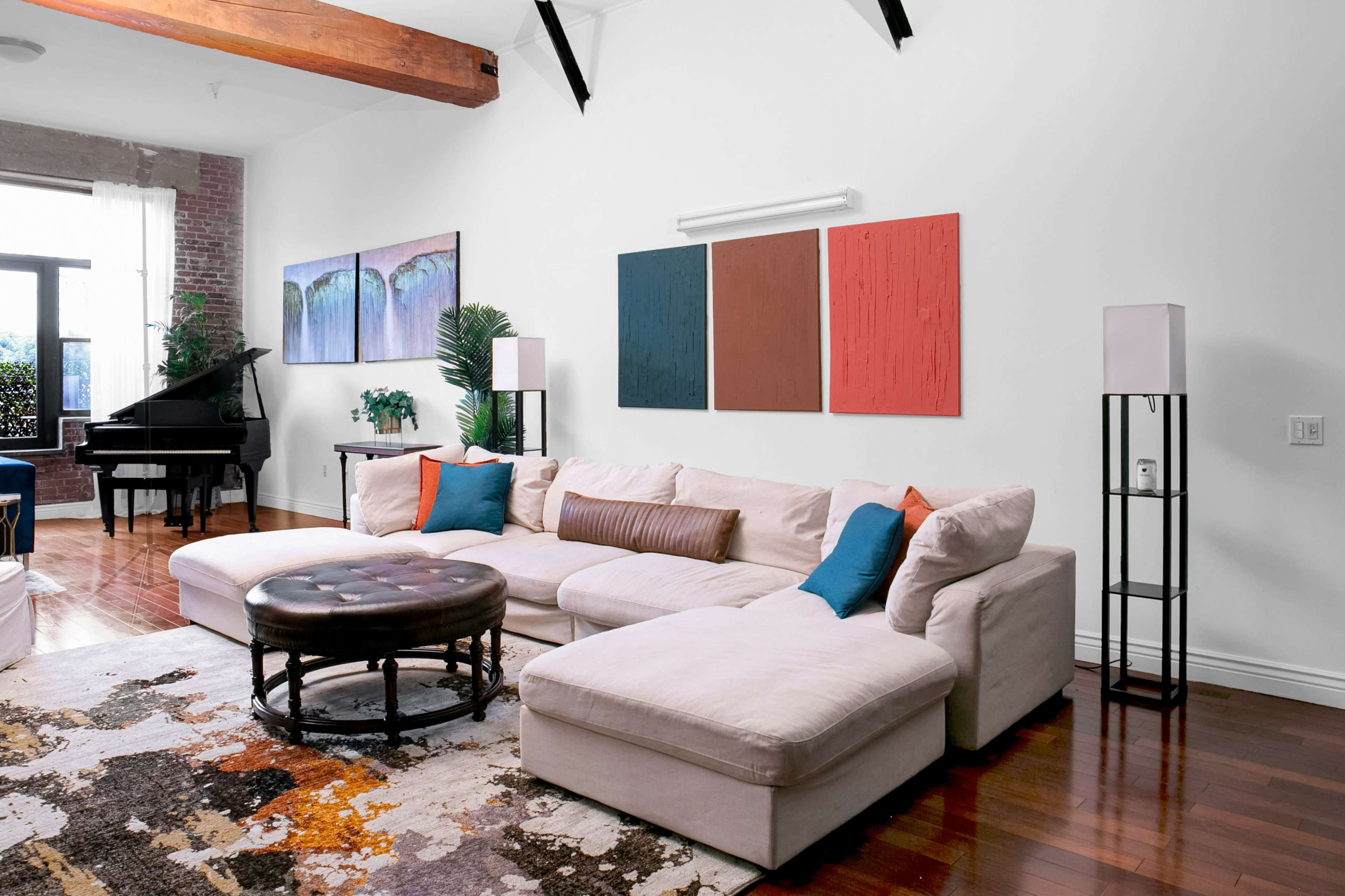 The image shows a living room with a sectional sofa, a round coffee table, two floor lamps, and abstract wall art above the couch.