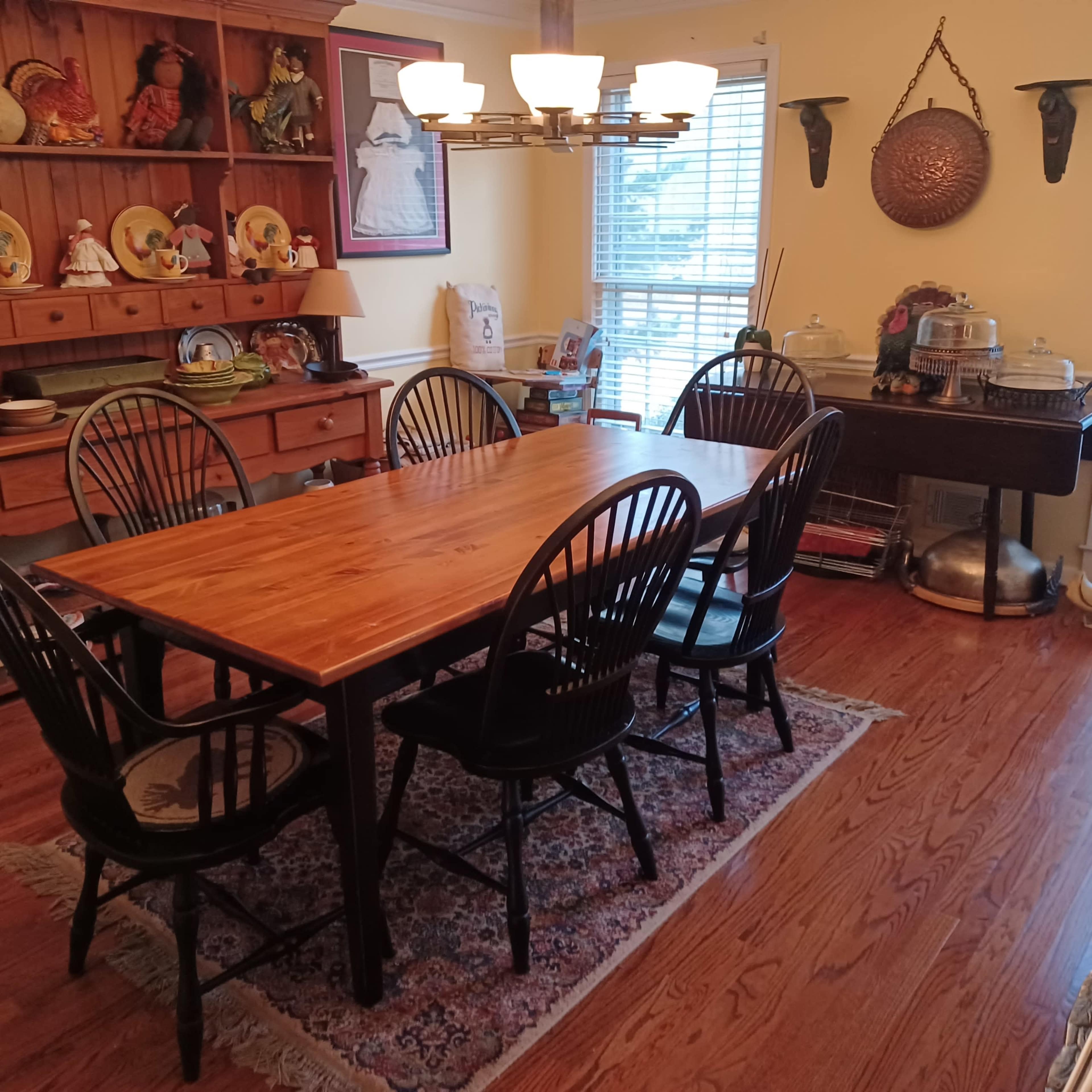 A dining room features a wooden table surrounded by six black chairs, with a shelf displaying decorative items on the wall.