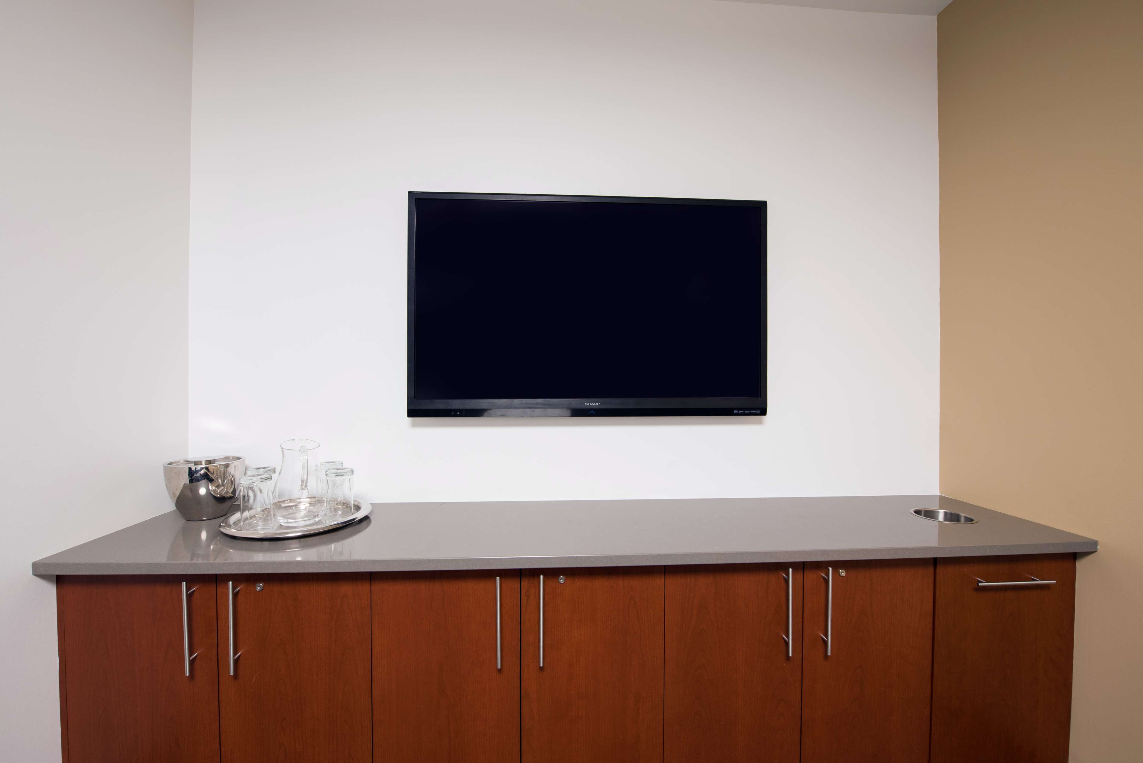 A modern meeting room with a wooden cabinet and a flat-screen TV mounted on the wall.
