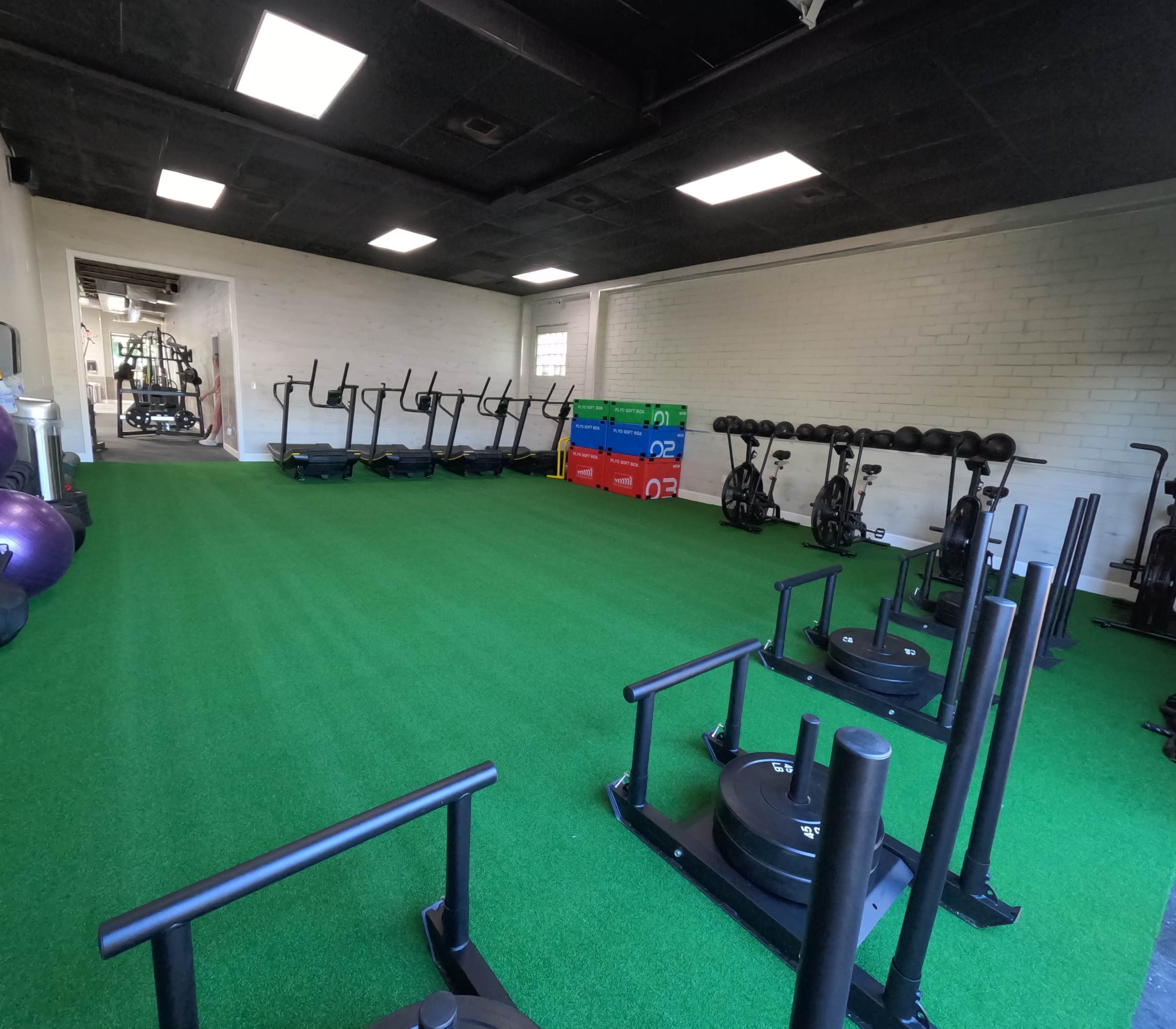 An indoor gym equipped with exercise machines, weights, and turf flooring.
