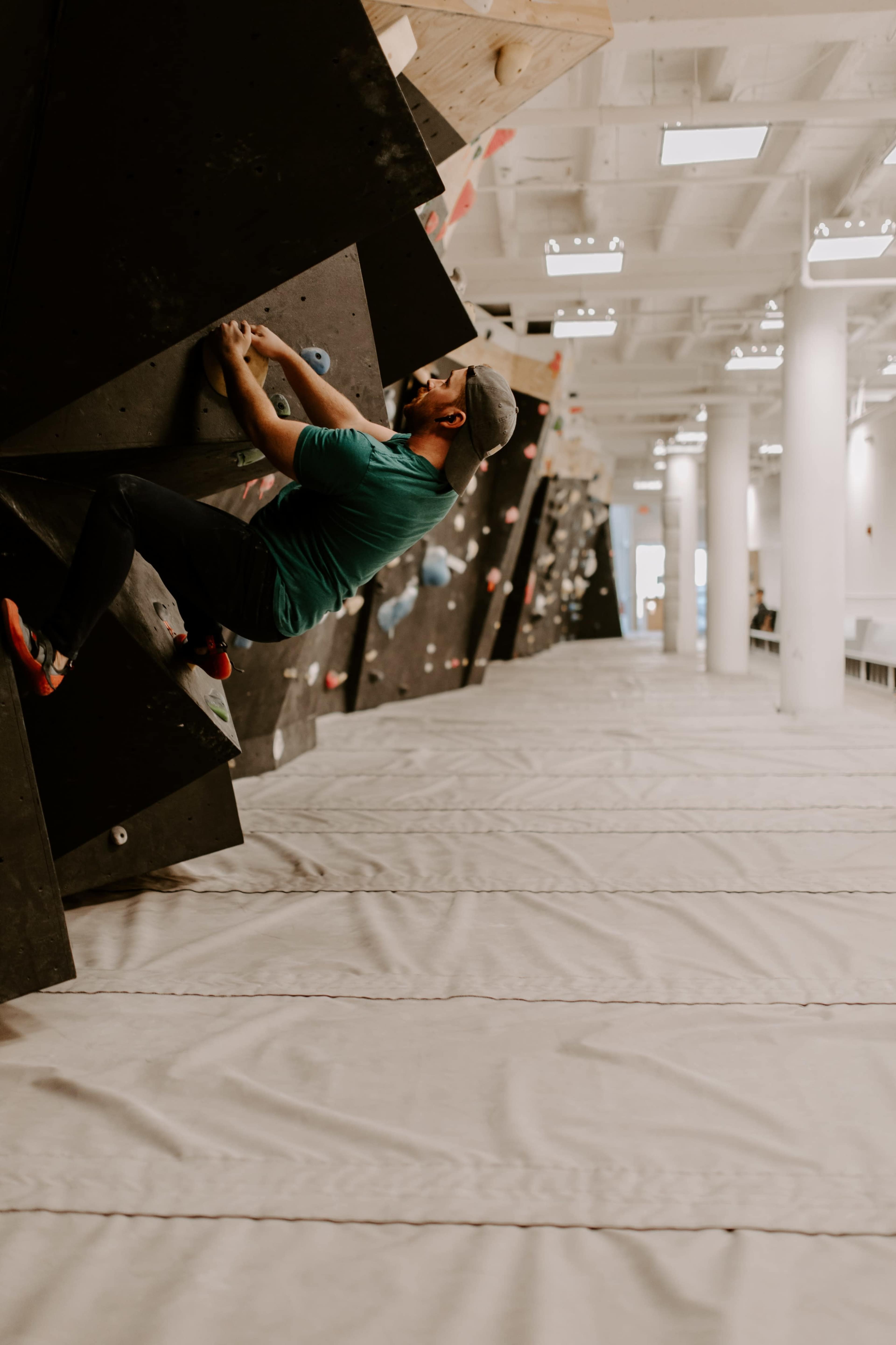 A climber scales a steep, angular bouldering wall in an indoor climbing gym.