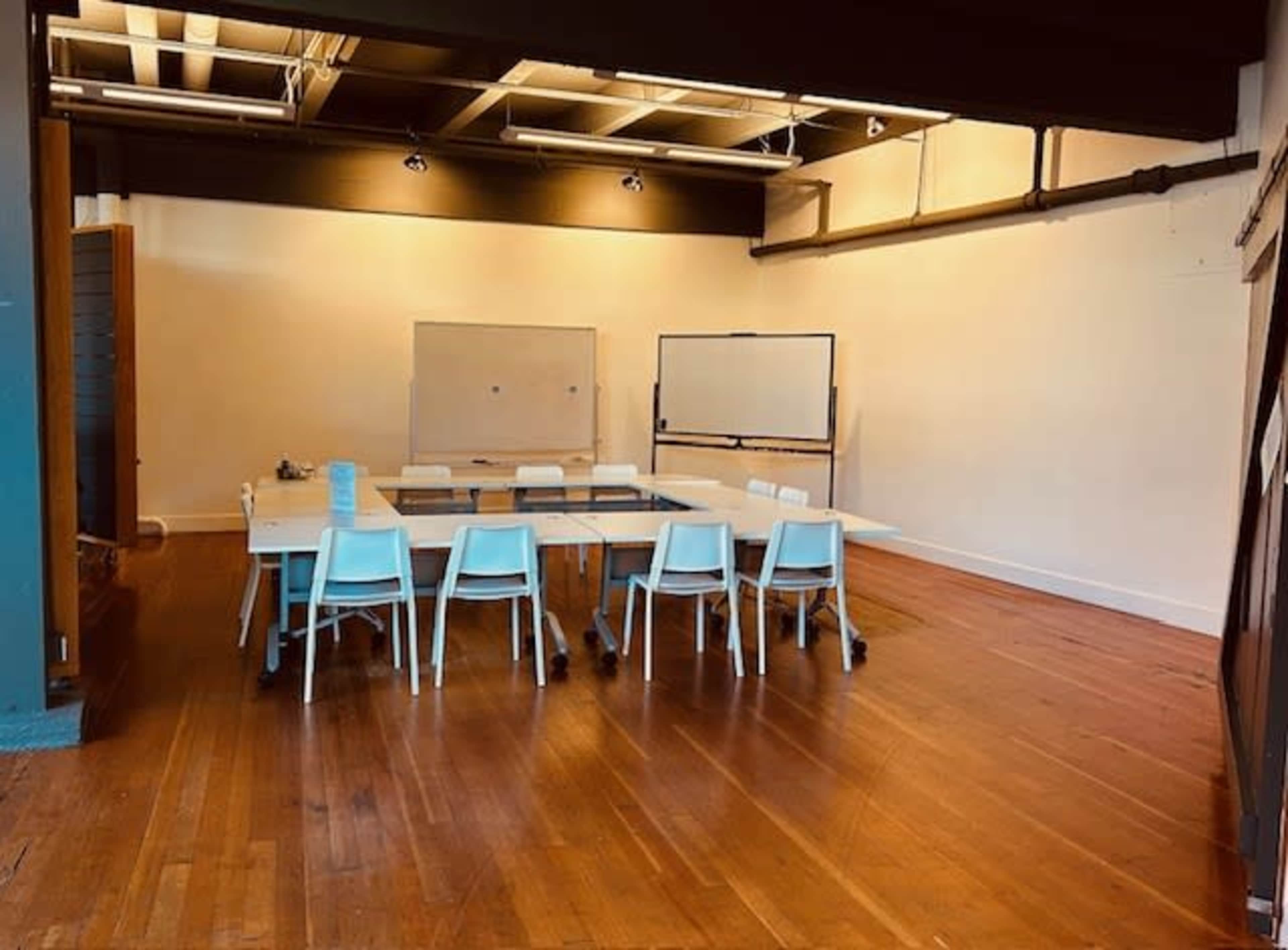 A large, empty conference room features a long table surrounded by light blue chairs and whiteboards on the walls.