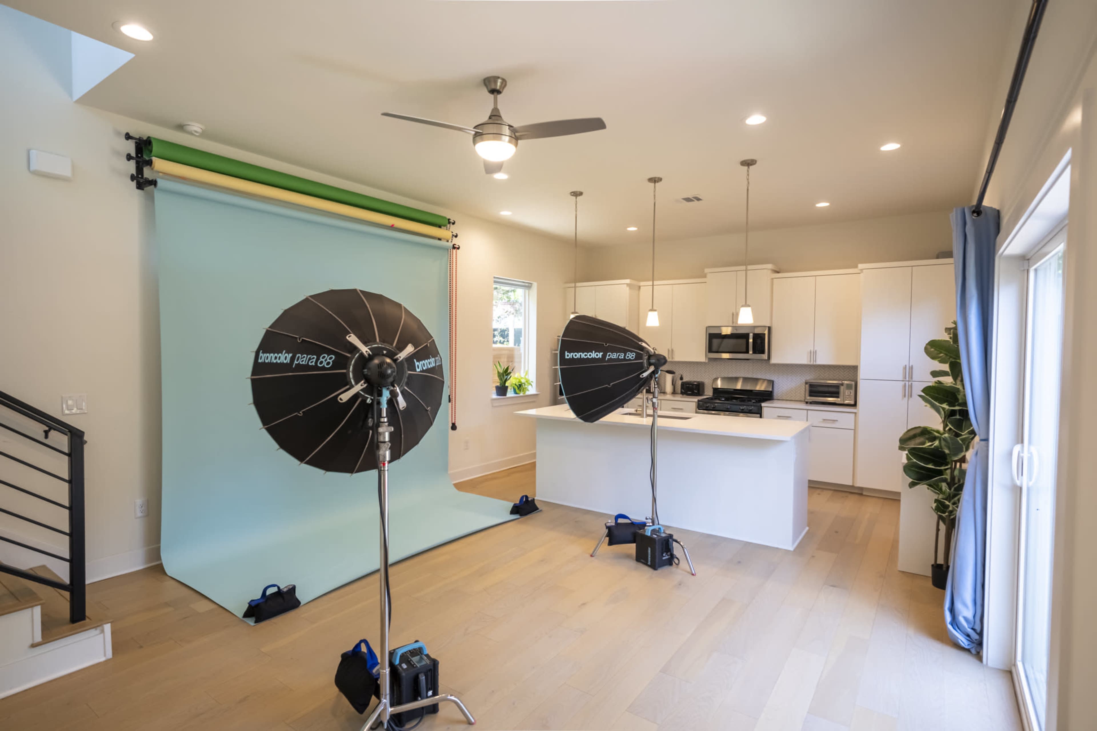 The image shows a kitchen with a green and blue backdrop set up for photography, featuring softbox lights and modern appliances.
