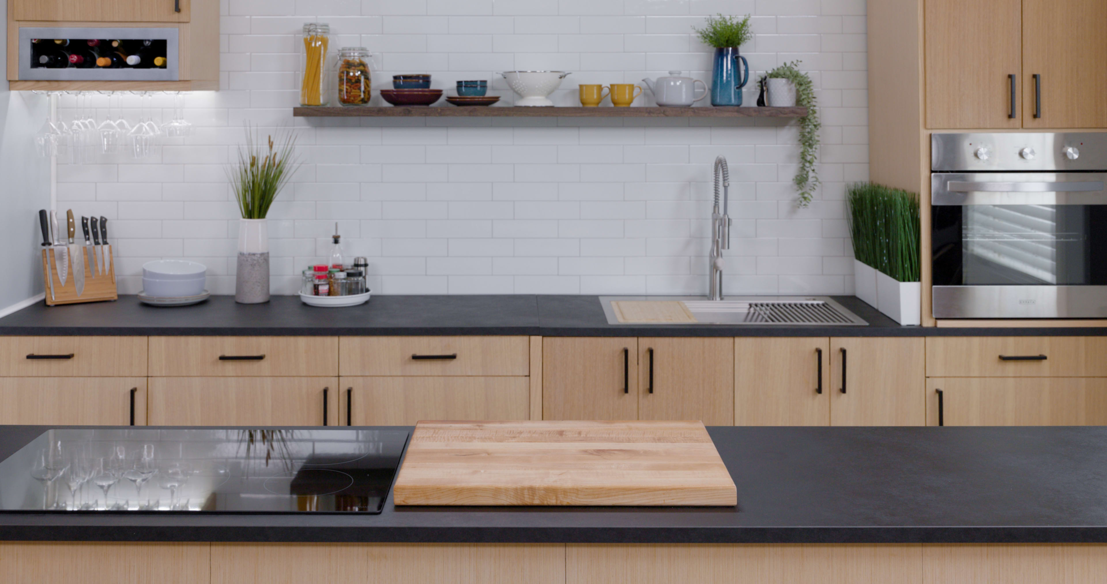 The image shows a modern kitchen with wooden cabinets, a black countertop, a sink, and a wooden cutting board on the island.