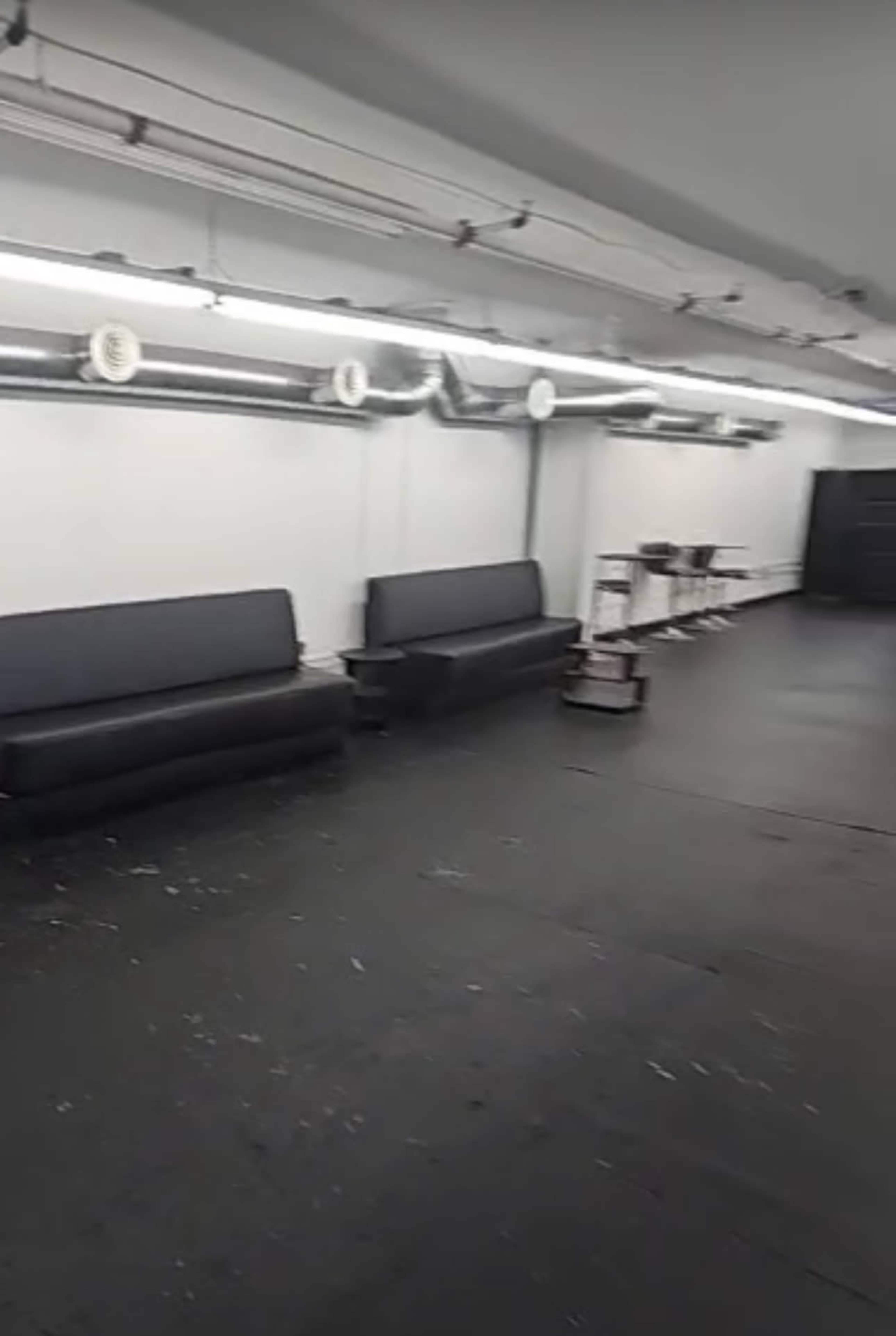 The image shows a spacious, empty room with black benches along one side and a shelf unit at the opposite end.