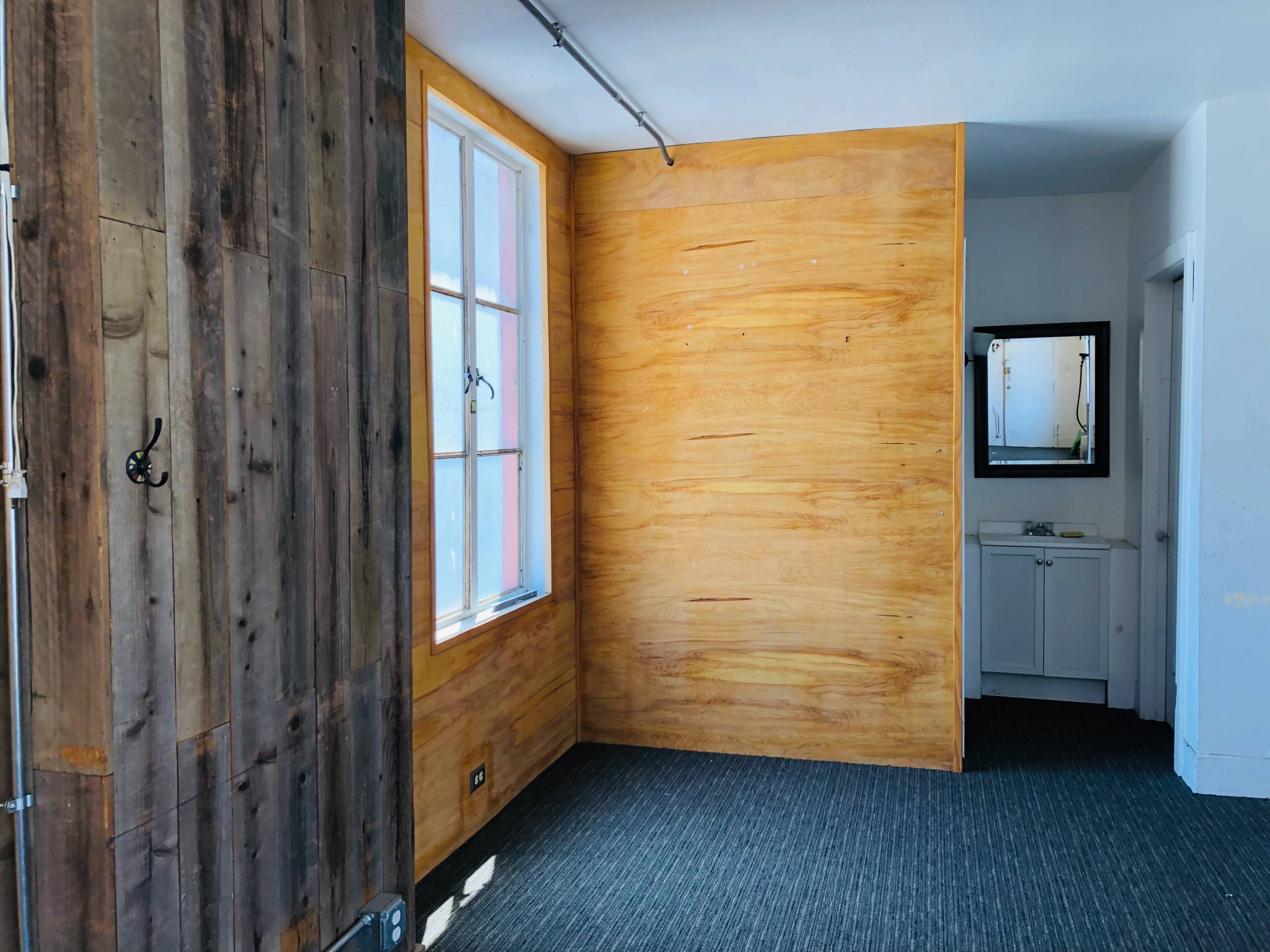 A room with wooden walls, a window, and a small bathroom area with a mirror and sink.
