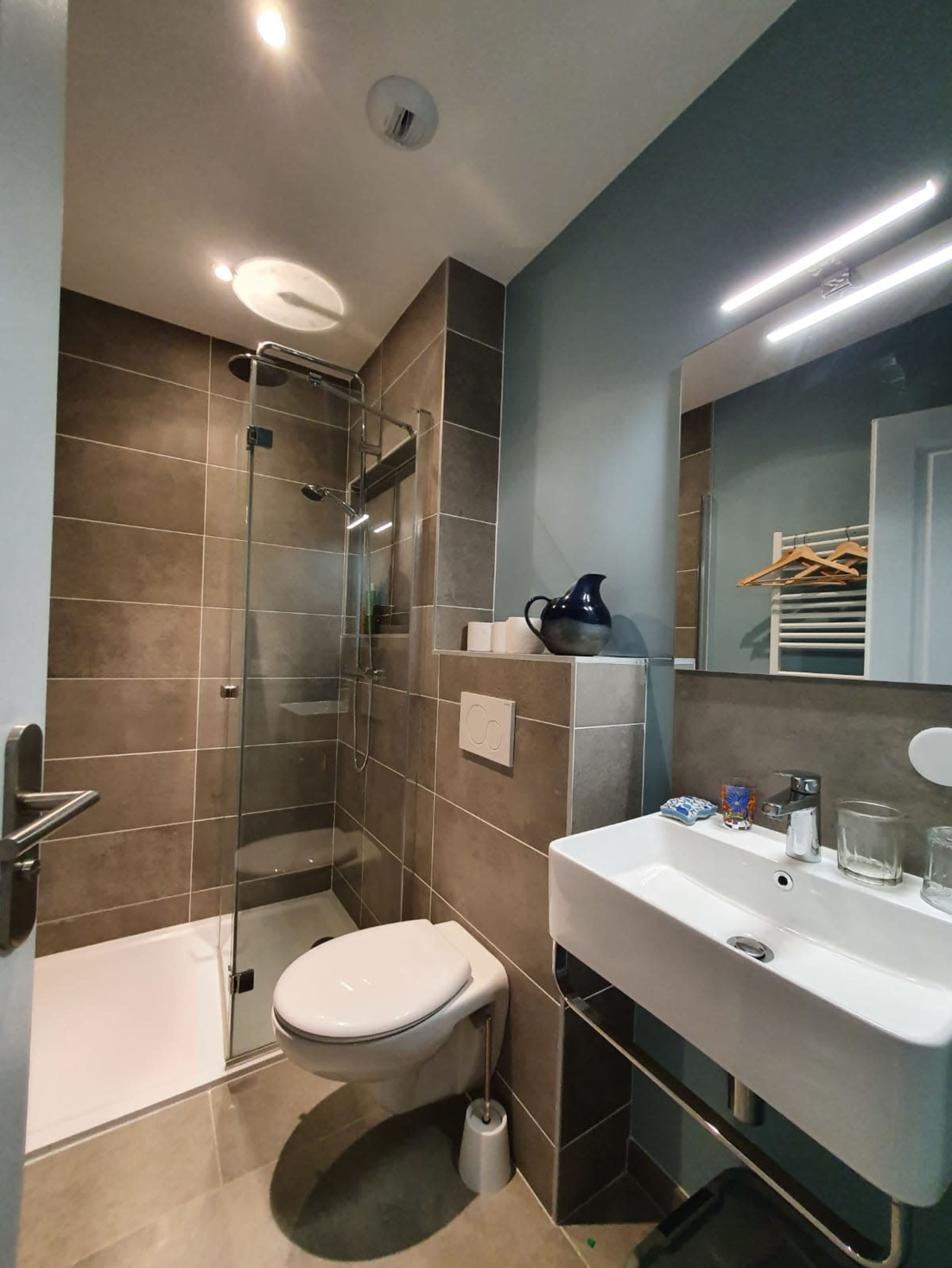 The image shows a modern bathroom featuring a glass shower enclosure, a toilet, and a wall-mounted sink with a mirror.