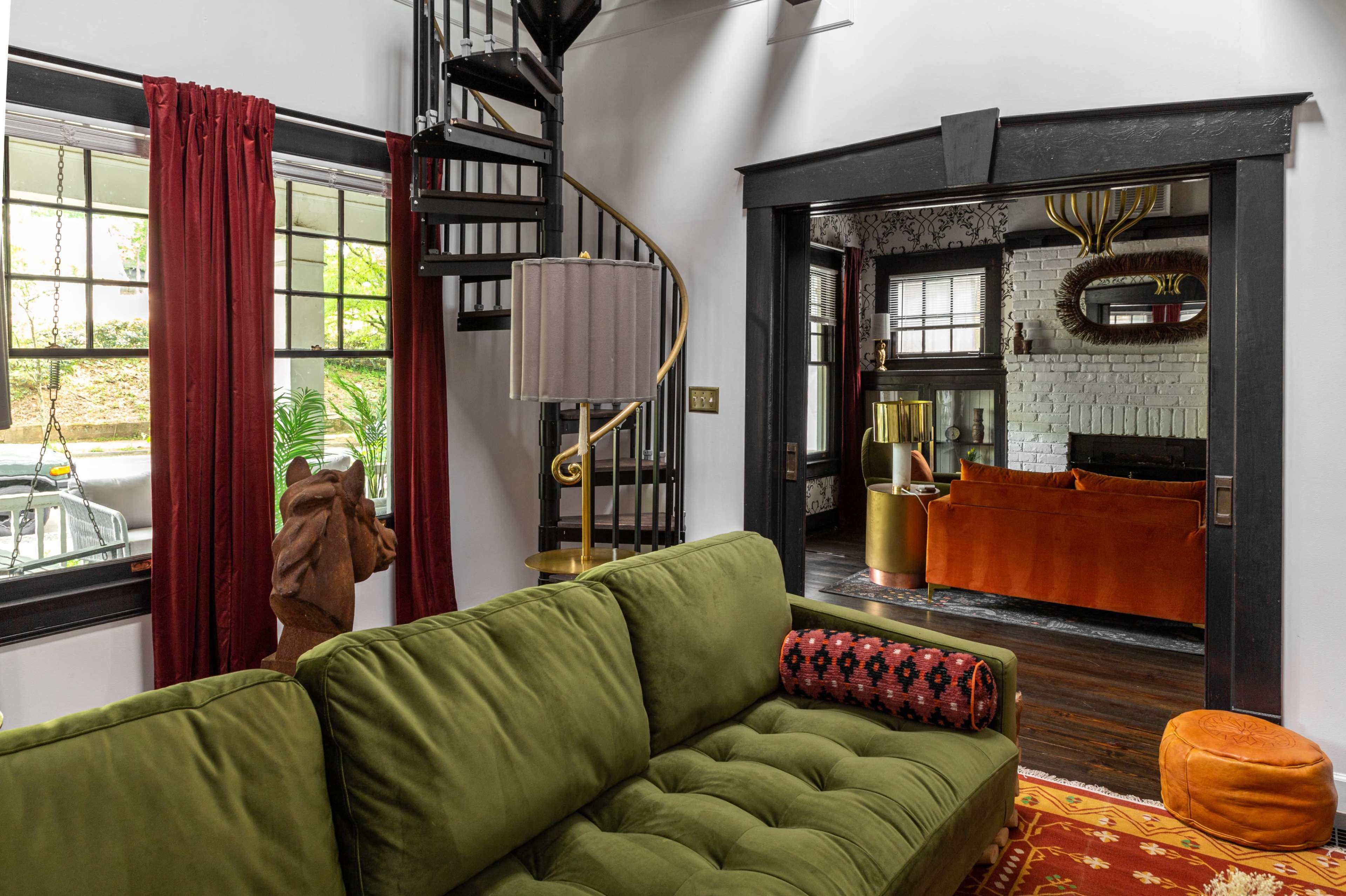 A cozy interior featuring a green sectional sofa, a spiral staircase, and orange accents in the adjoining room.