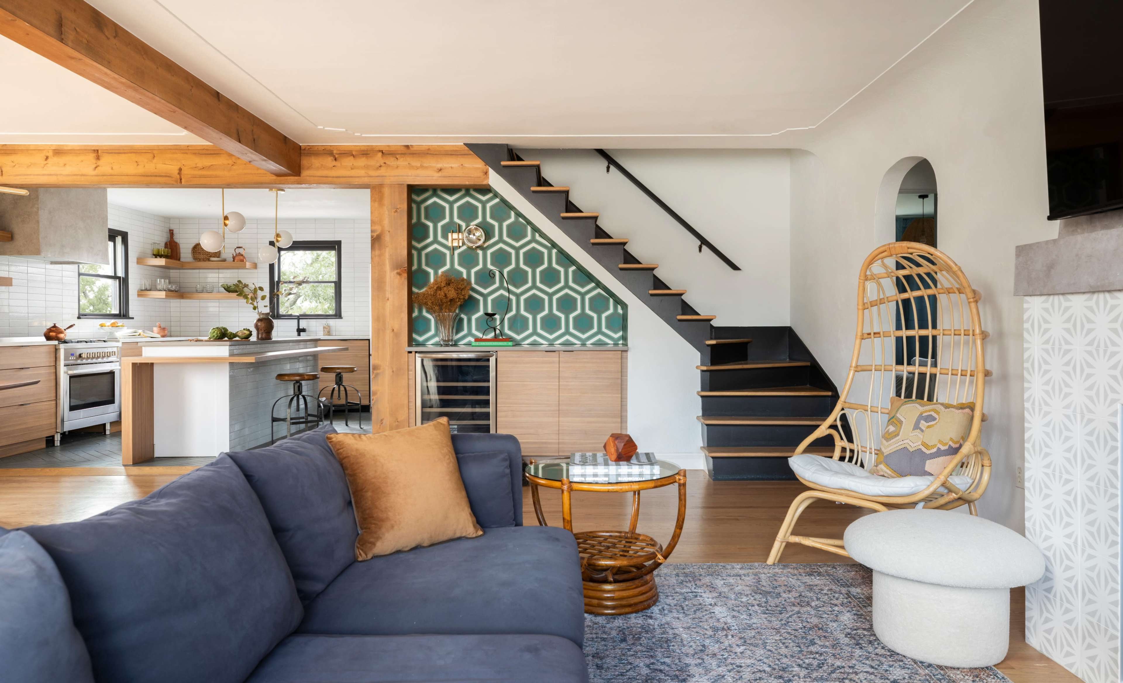 The image shows a modern living room featuring a blue sofa, a round glass coffee table, and a staircase with a patterned wall behind it, leading to the upper level.