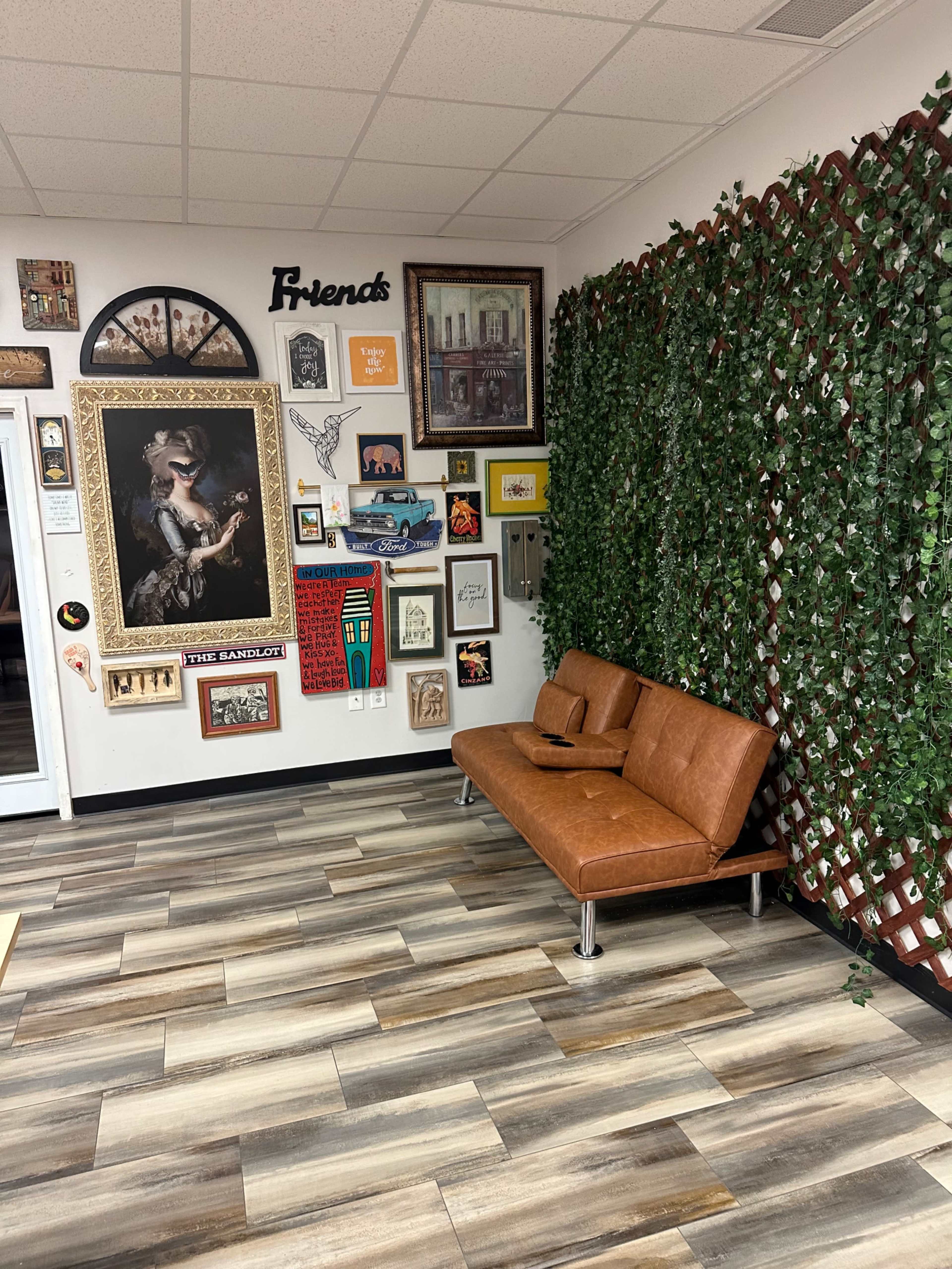 A cozy waiting area features a brown leather sofa against a wall adorned with various framed artworks and greenery.