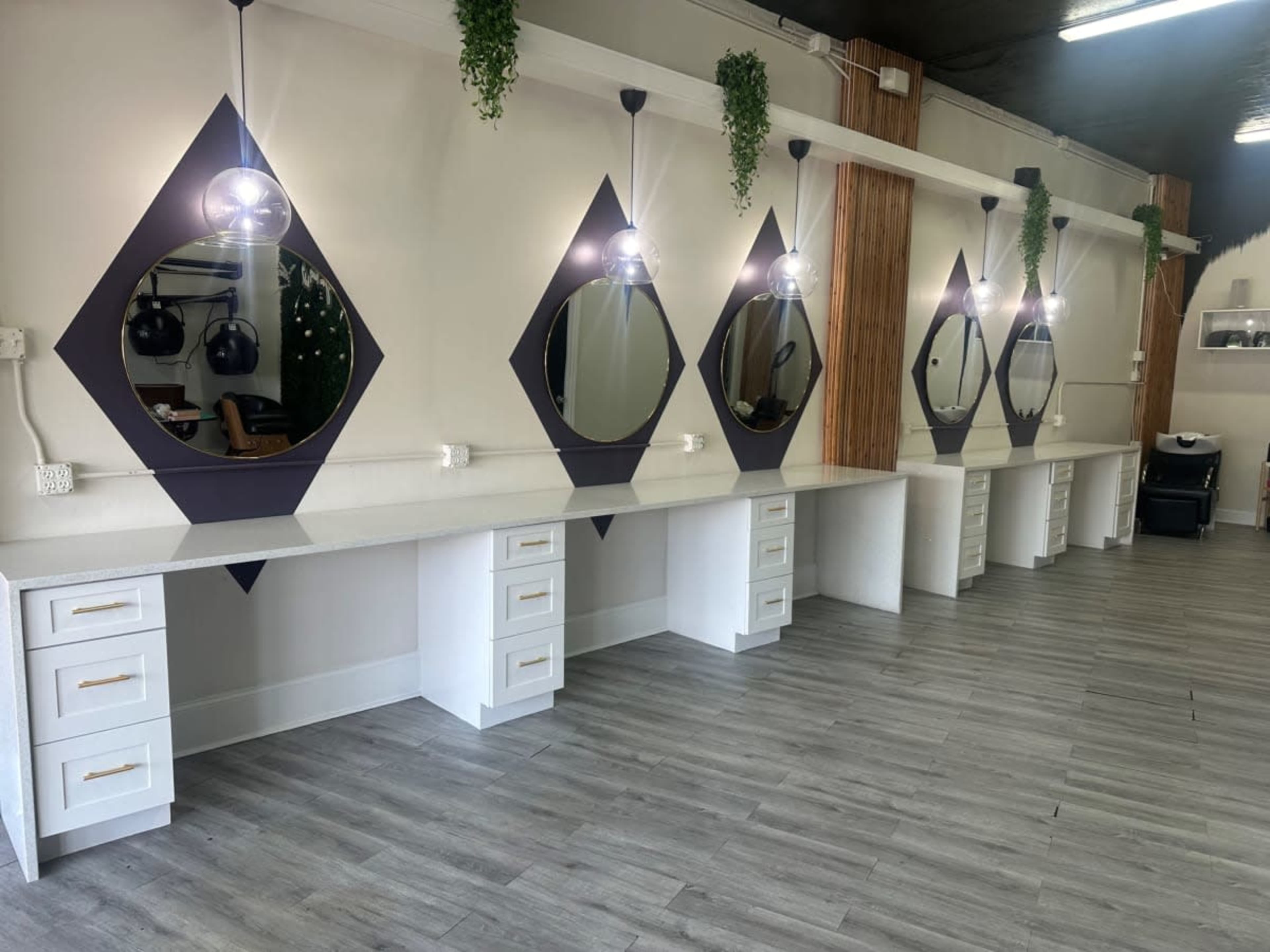 The image shows a salon interior with four workstations, each featuring a wall-mounted mirror and storage drawers underneath.