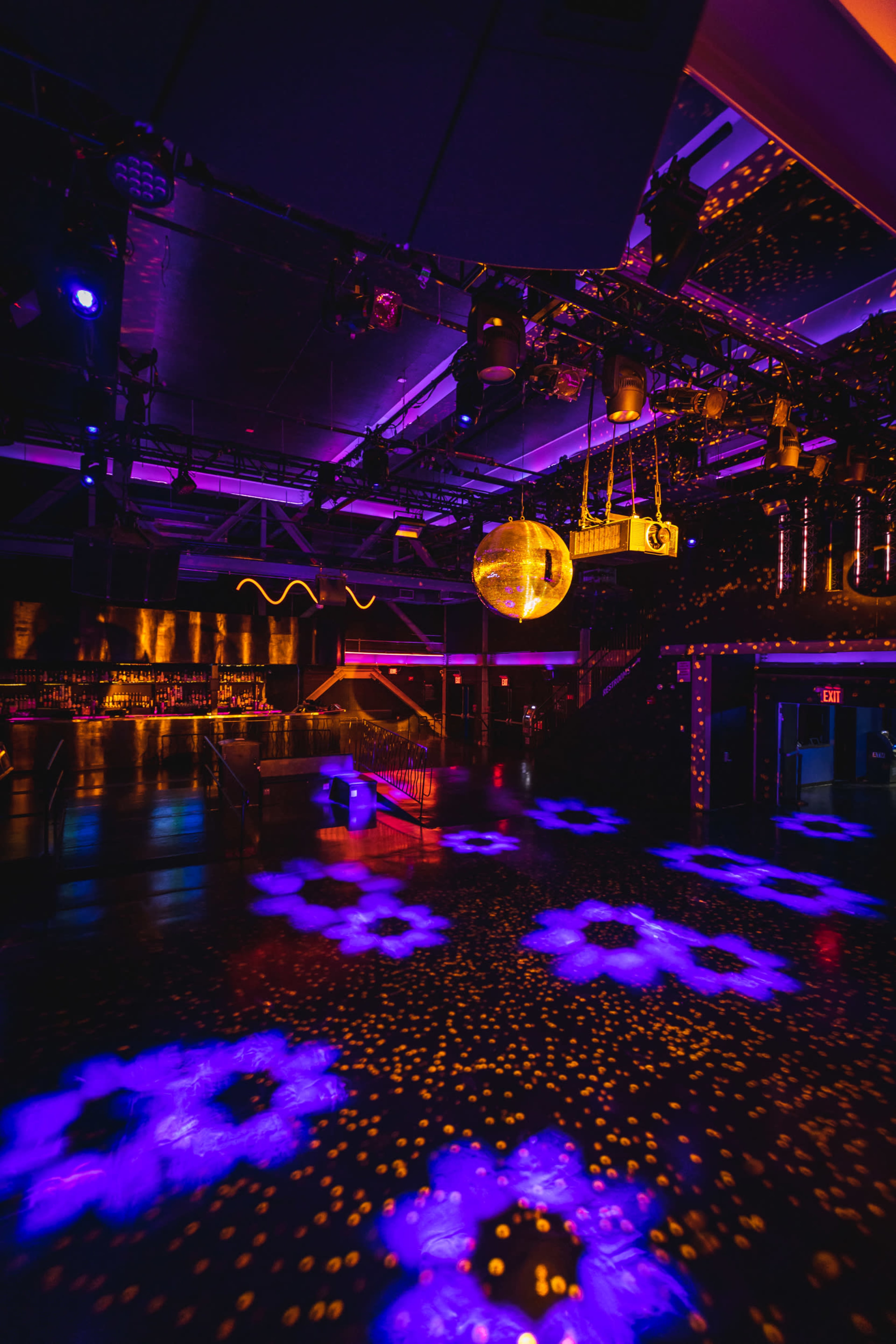 The image shows a vibrant nightclub interior with colorful lighting, a disco ball hanging from the ceiling, and illuminated patterns on the dance floor.