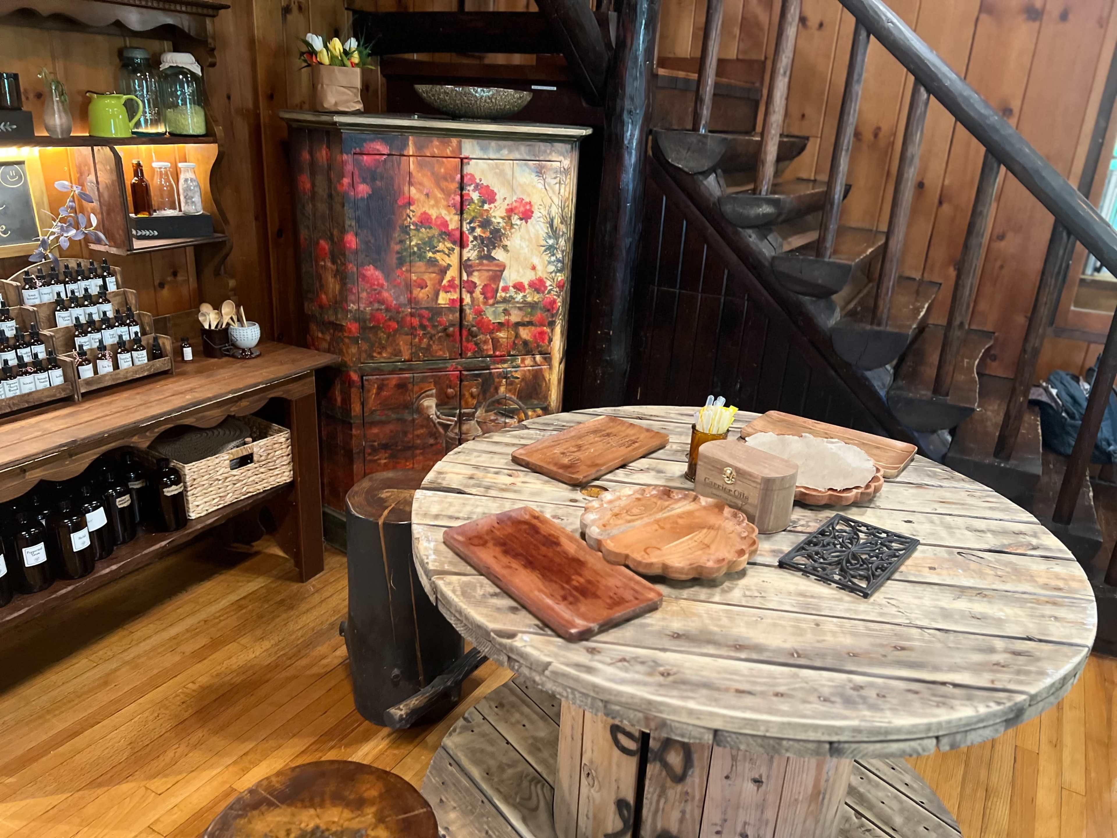 A rustic wooden table with wooden platters and a metal decorative piece is placed near an artistic cabinet and a staircase in a cozy interior space.