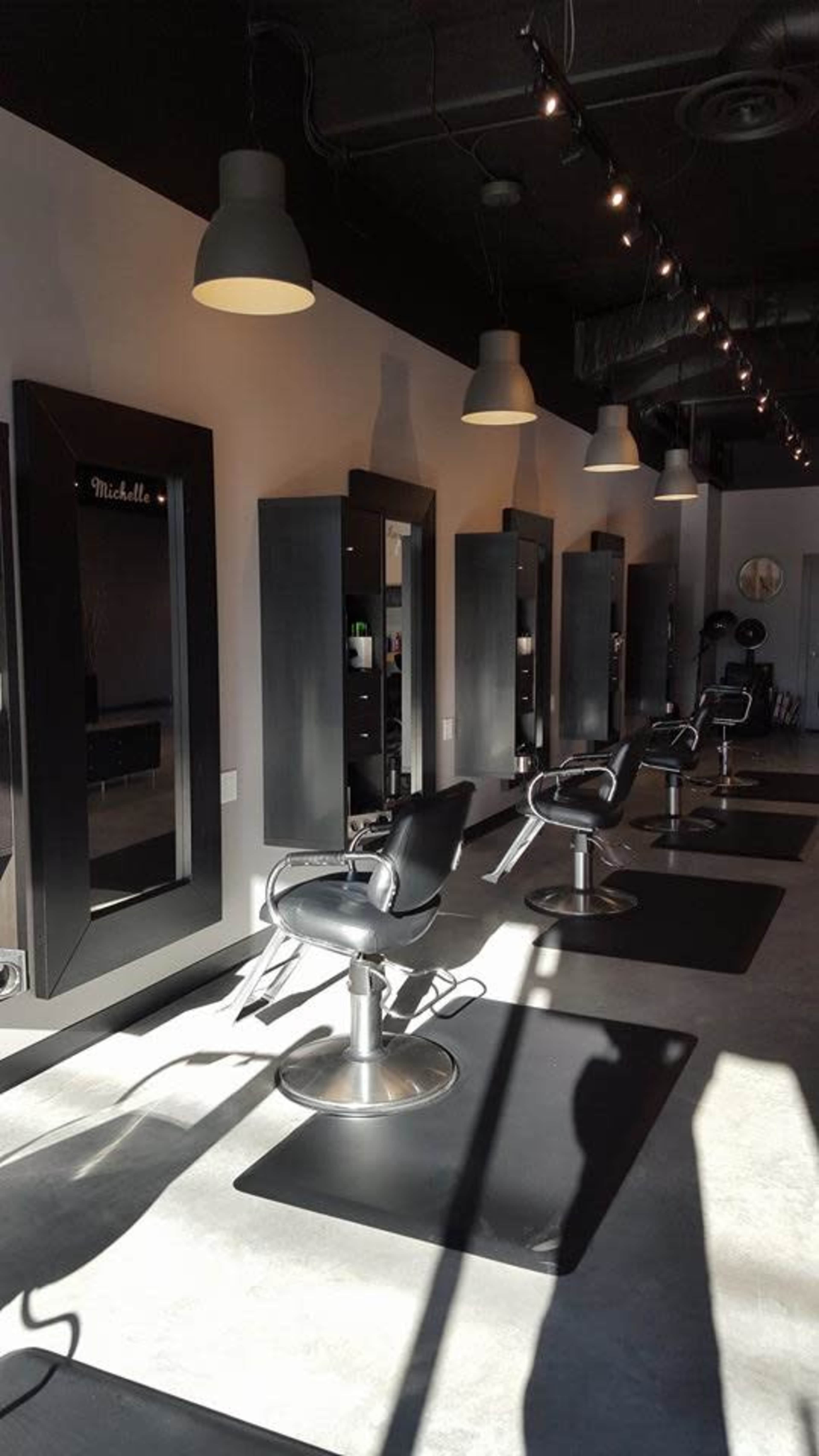 The image shows a modern hair salon with five stylist stations, each featuring a large mirror and a black salon chair, arranged in a well-lit space.