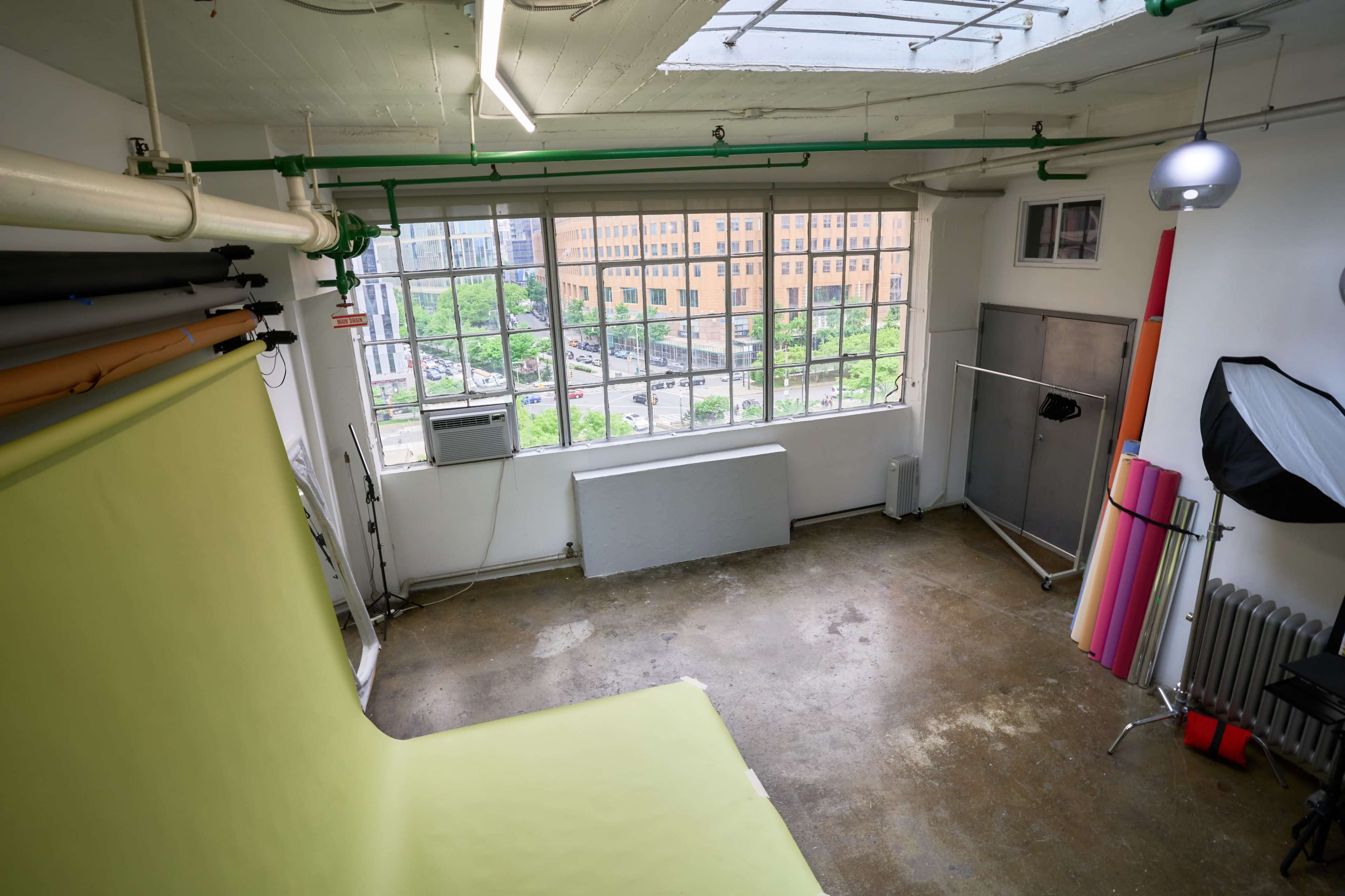 A photography studio with large windows, green and pink backdrops, and industrial-style flooring.