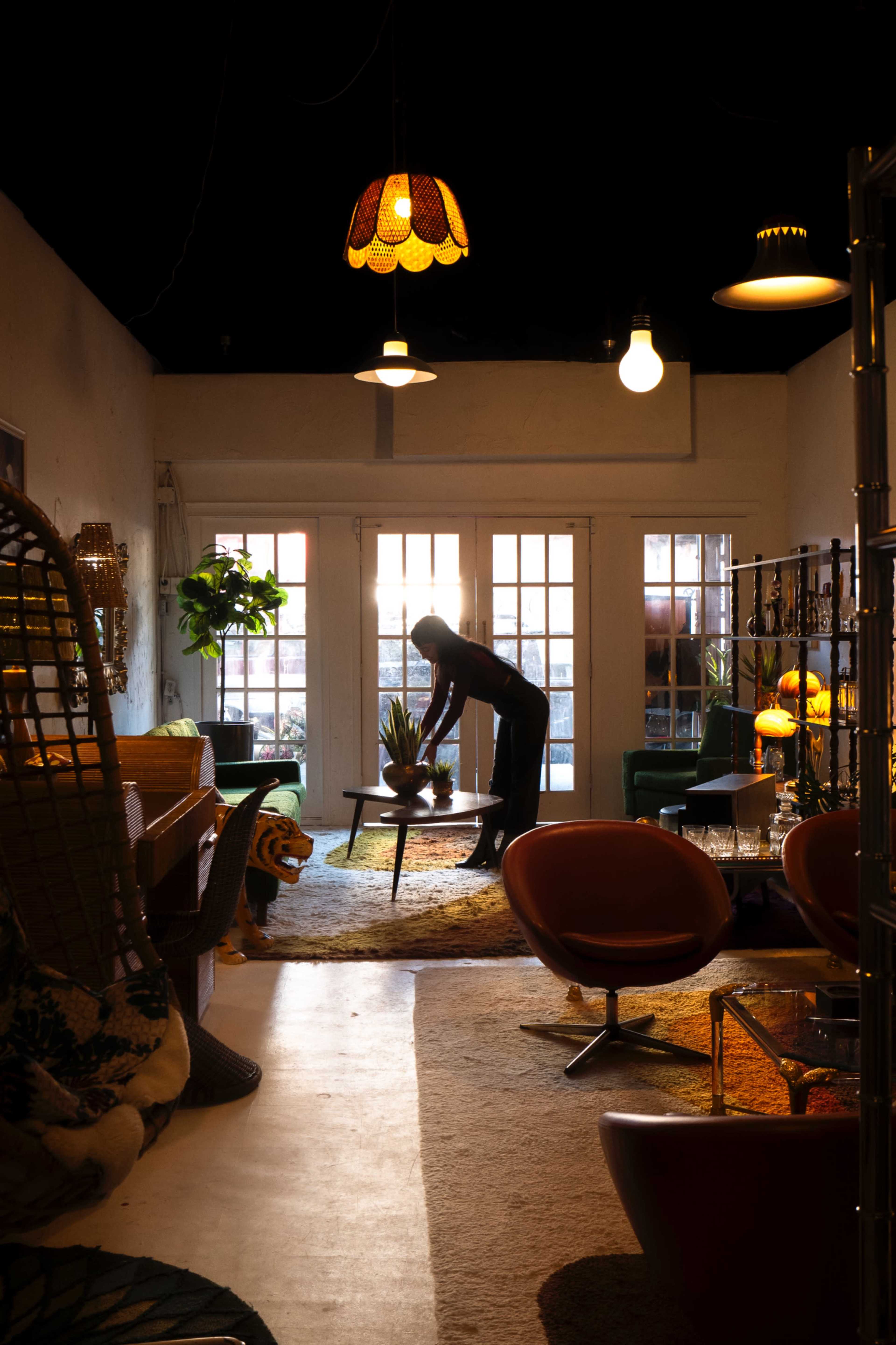 A person is arranging a plant on a table in a well-decorated room featuring vibrant furniture and indoor plants.