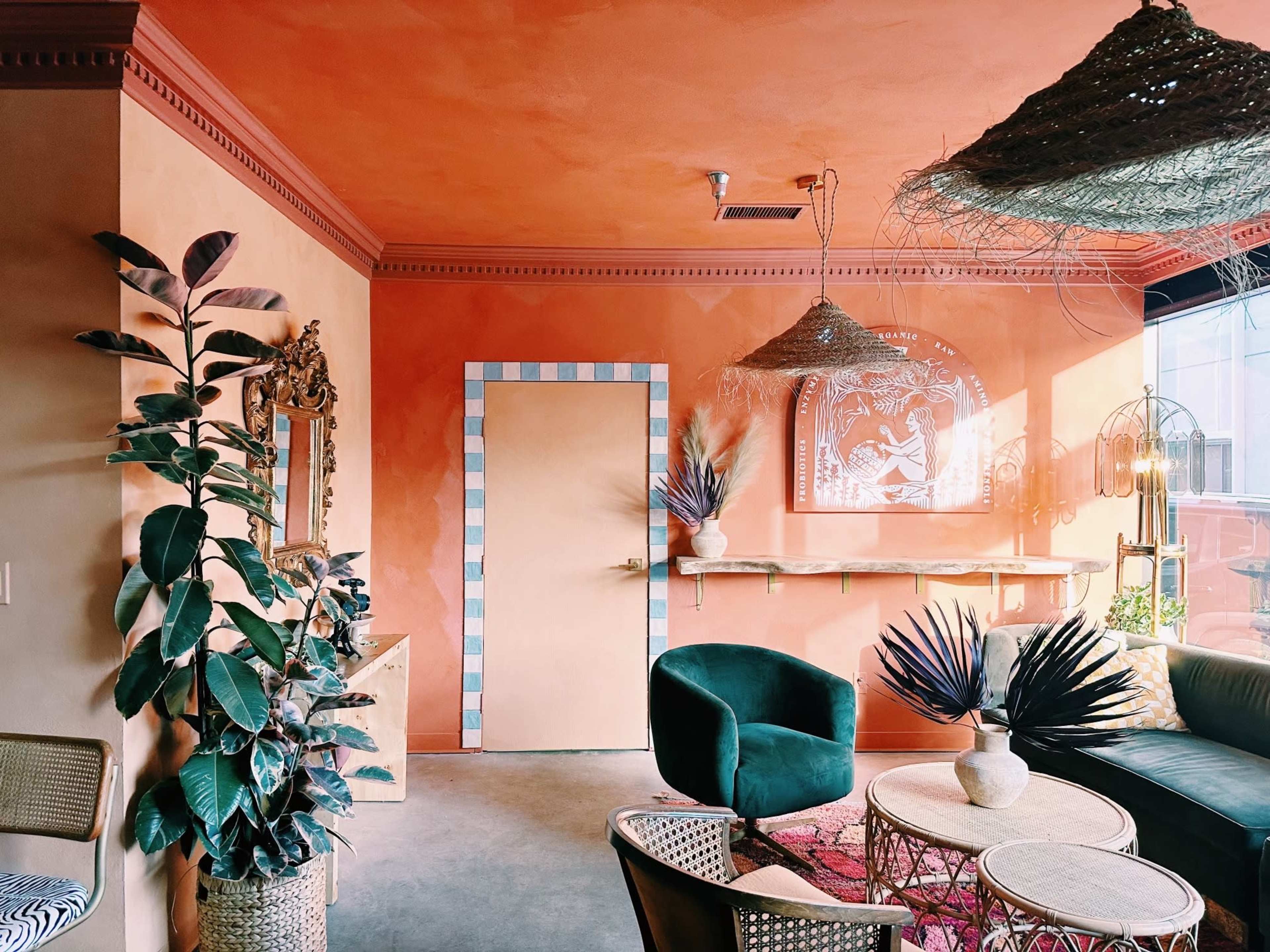 A brightly colored interior room with orange walls, green furniture, decorative plants, and woven light fixtures.