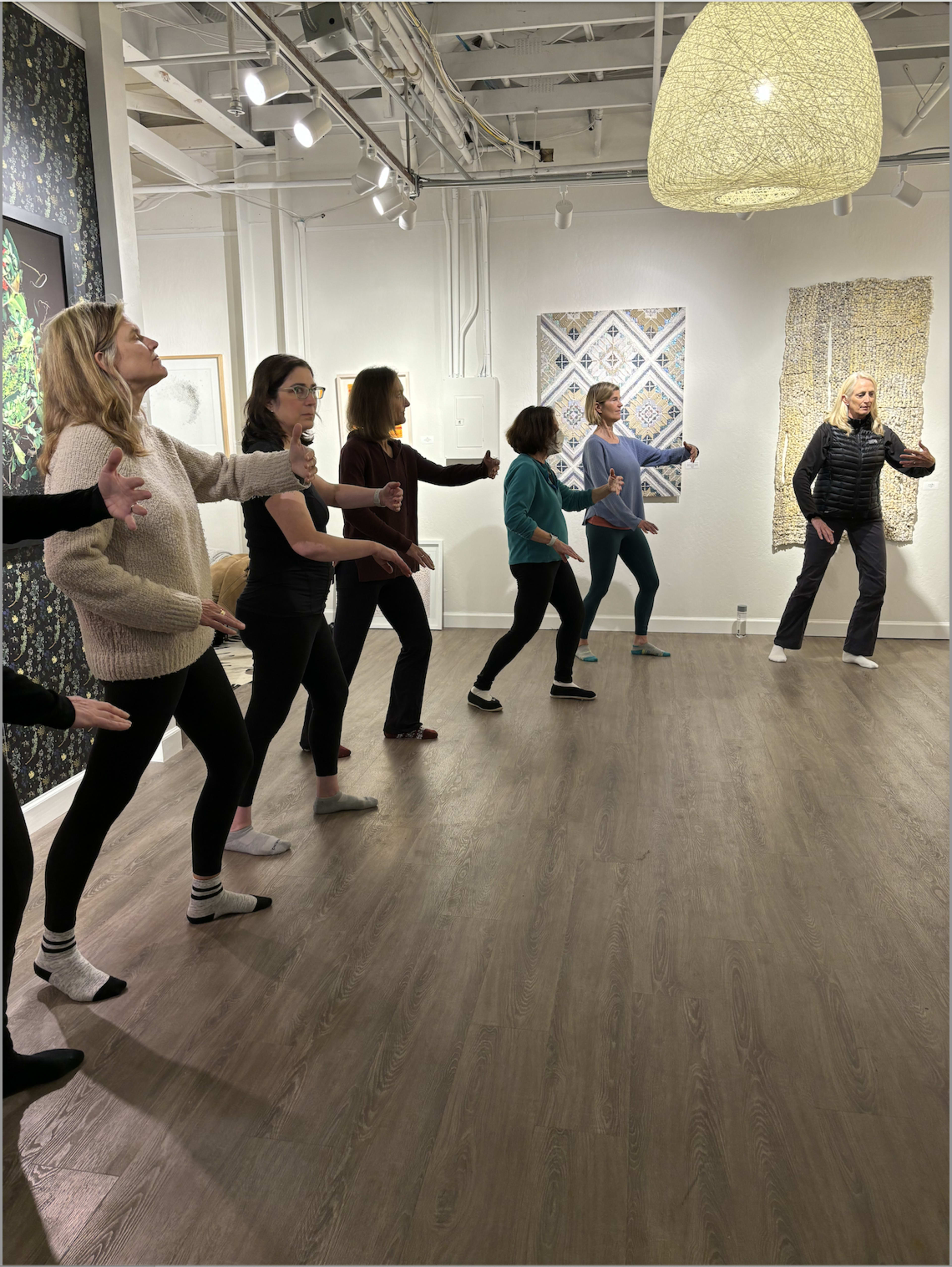 A group of people performs a dance or movement exercise in an art gallery surrounded by various artworks.