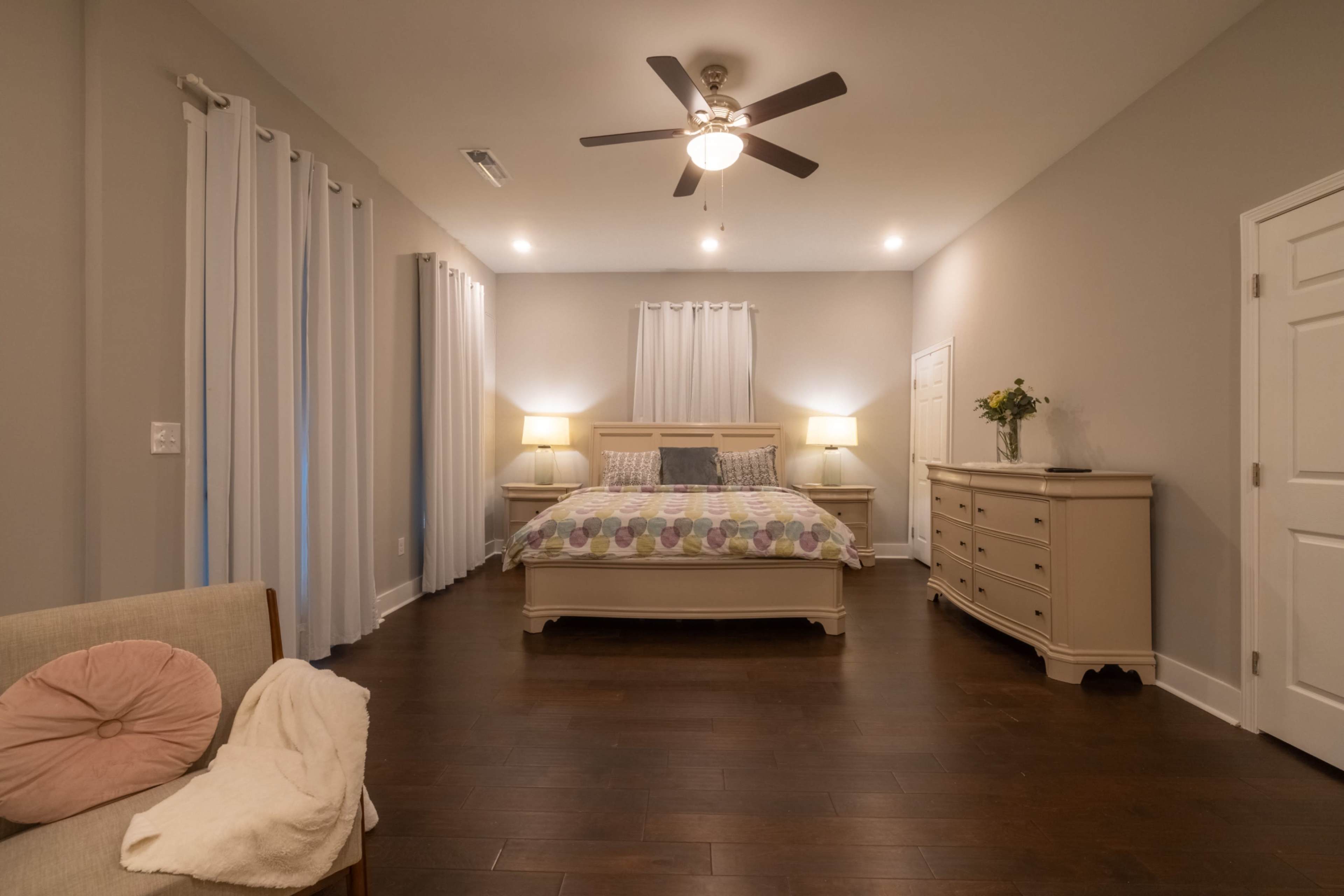 A well-designed bedroom featuring a large bed with a patterned comforter, flanked by two lamps, and a chest of drawers against the wall.