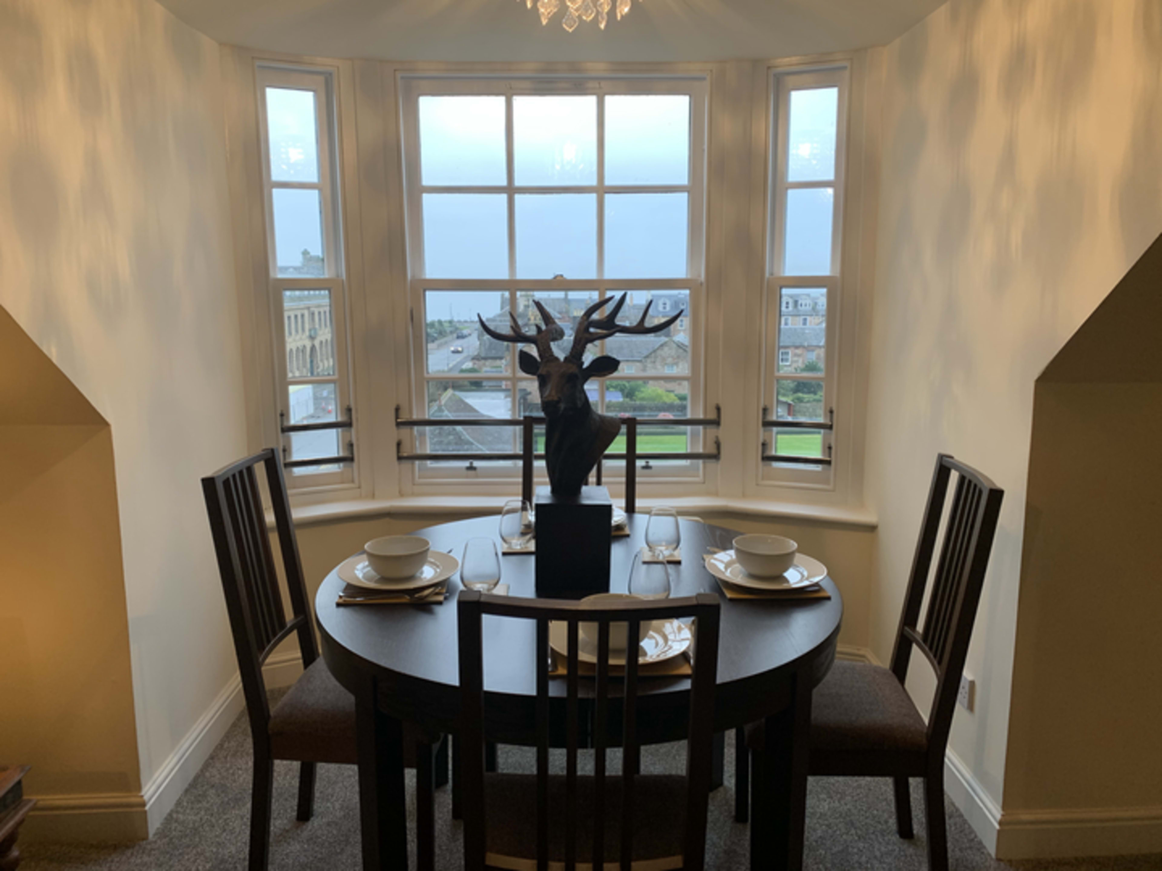 A small dining area features a round table set for two, with a large window providing a view of the landscape outside.
