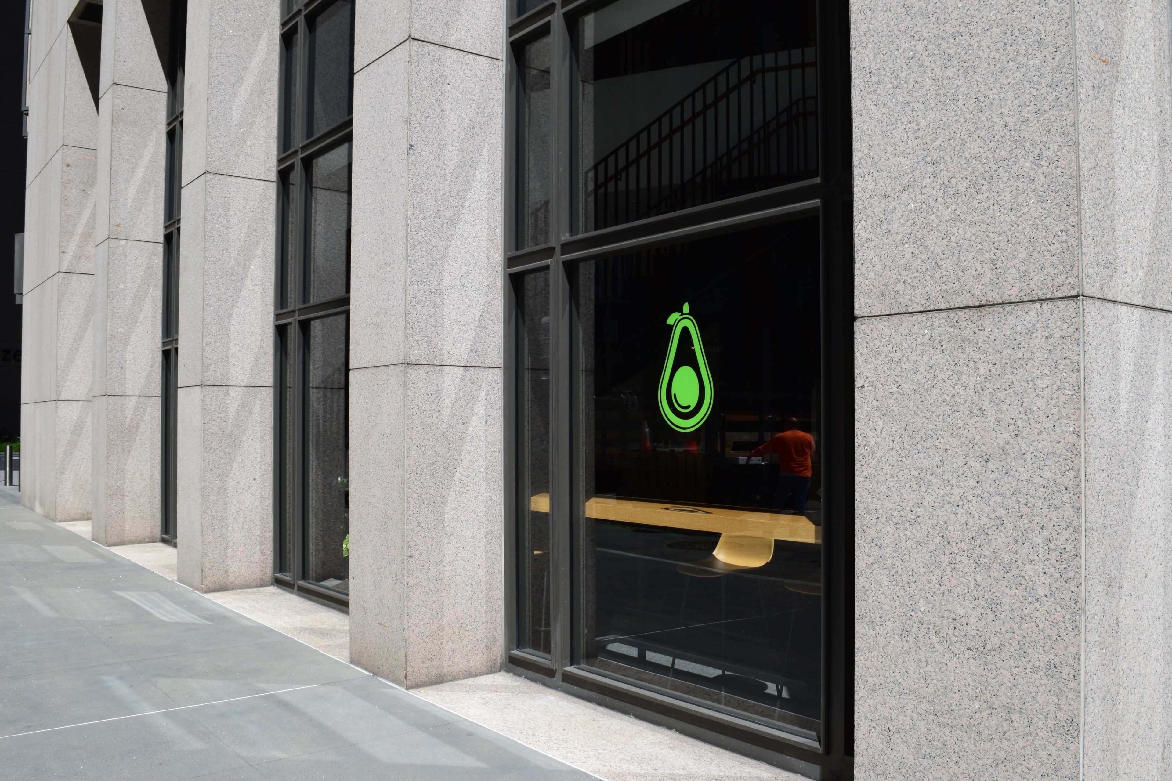 A large window with a green avocado logo is set in a granite facade of a building.