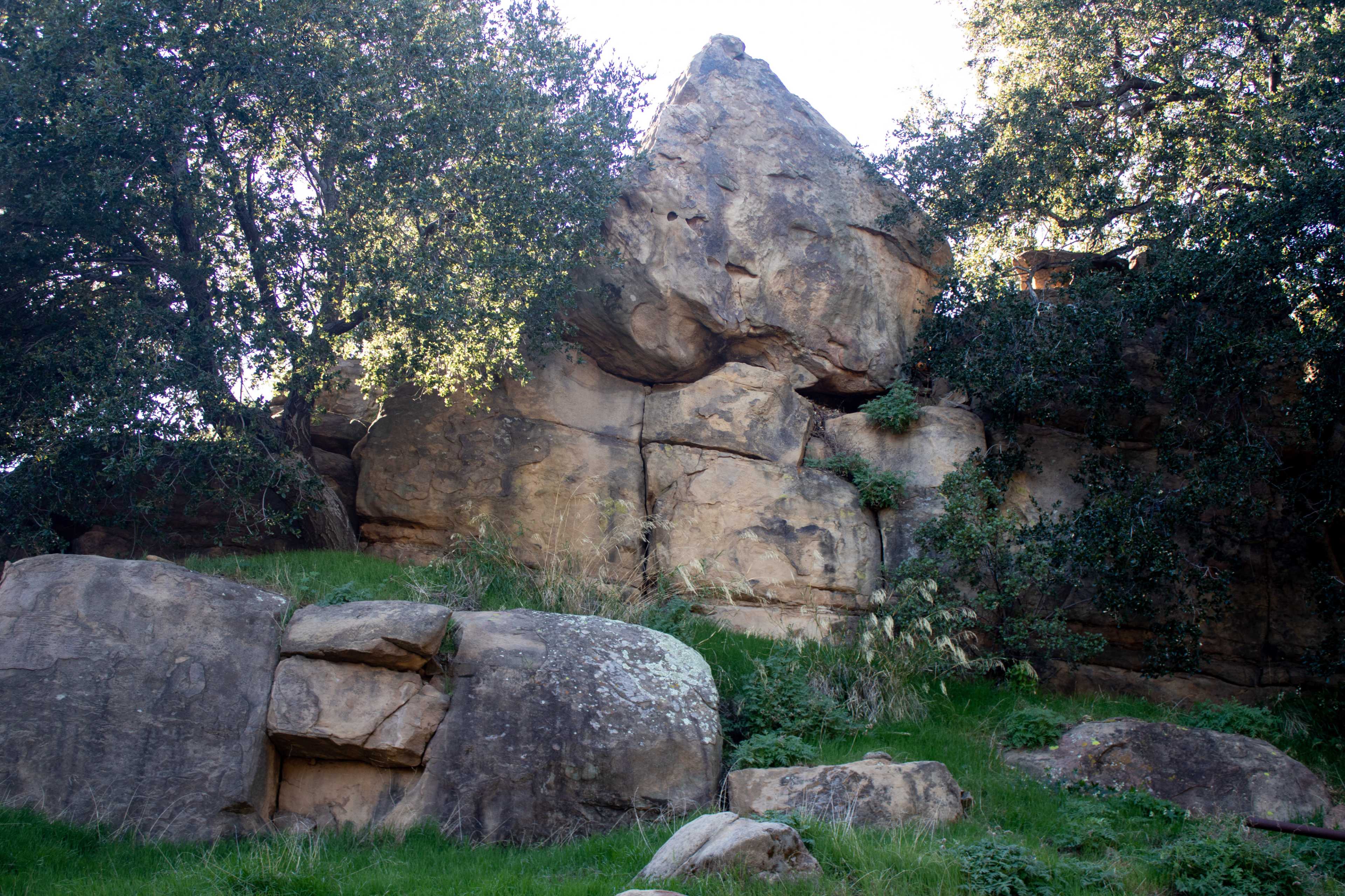 A rocky hillside with large boulders and scattered greenery under a clear sky.