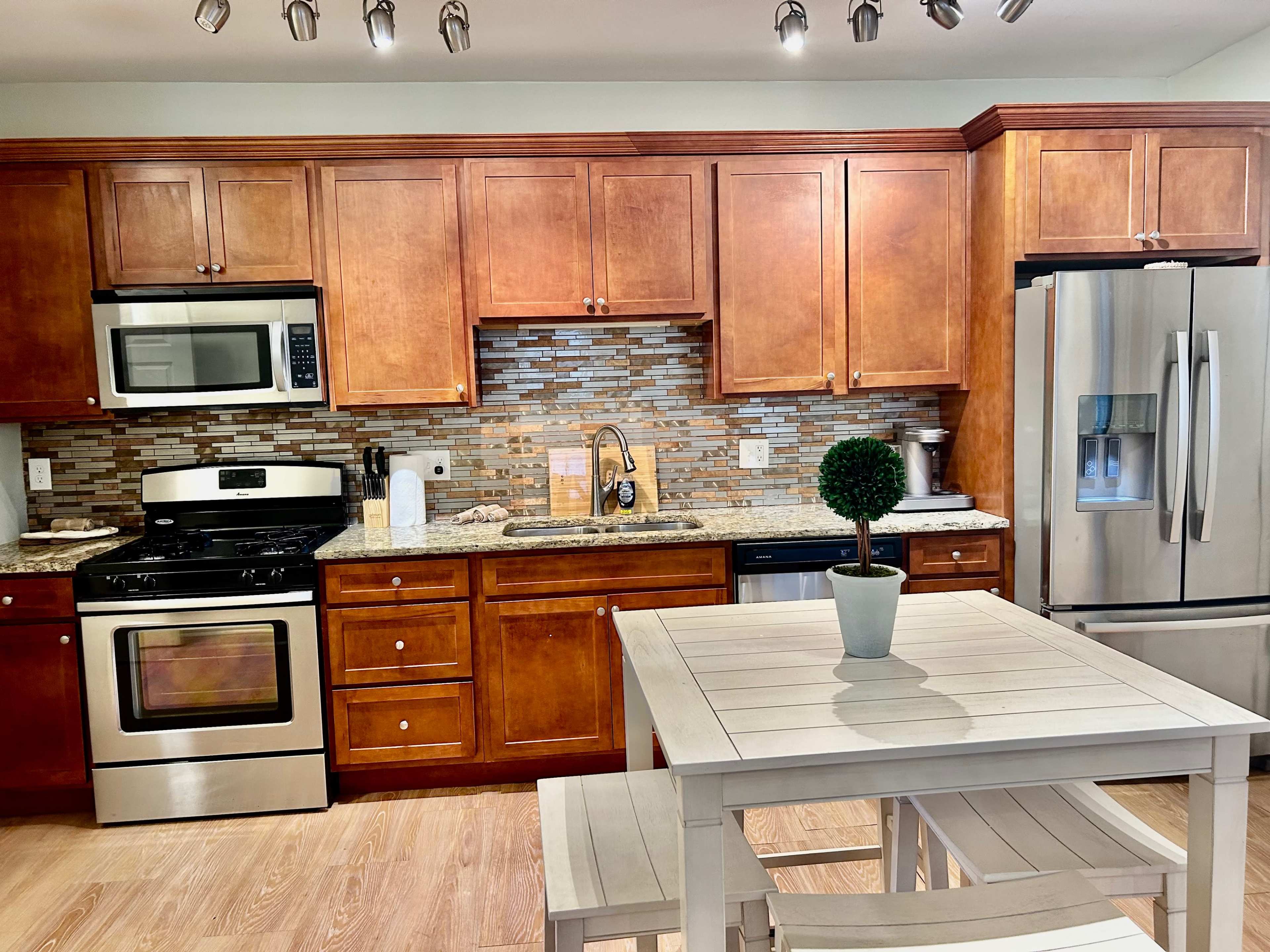 A kitchen with wooden cabinets, stainless steel appliances, a tiled backsplash, and a small dining table with a potted plant.