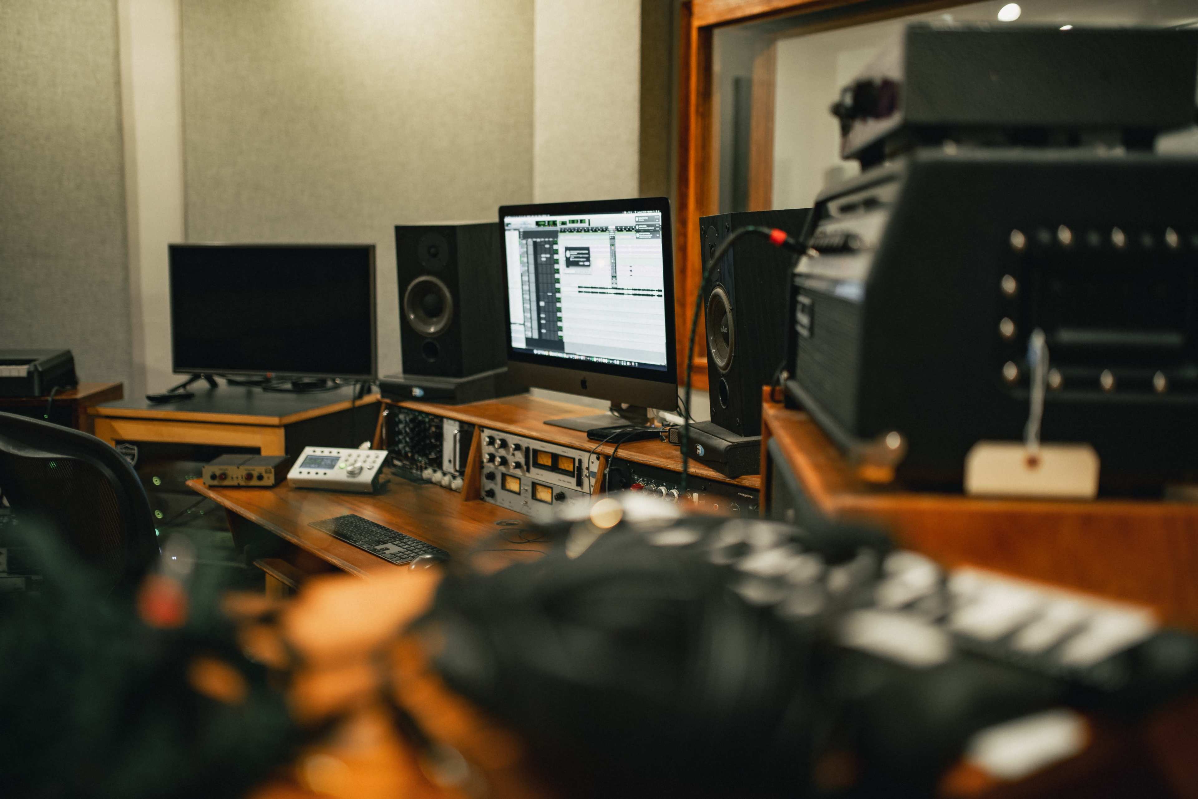 A recording studio setup with a computer, audio equipment, and various recording devices arranged on wooden furniture.