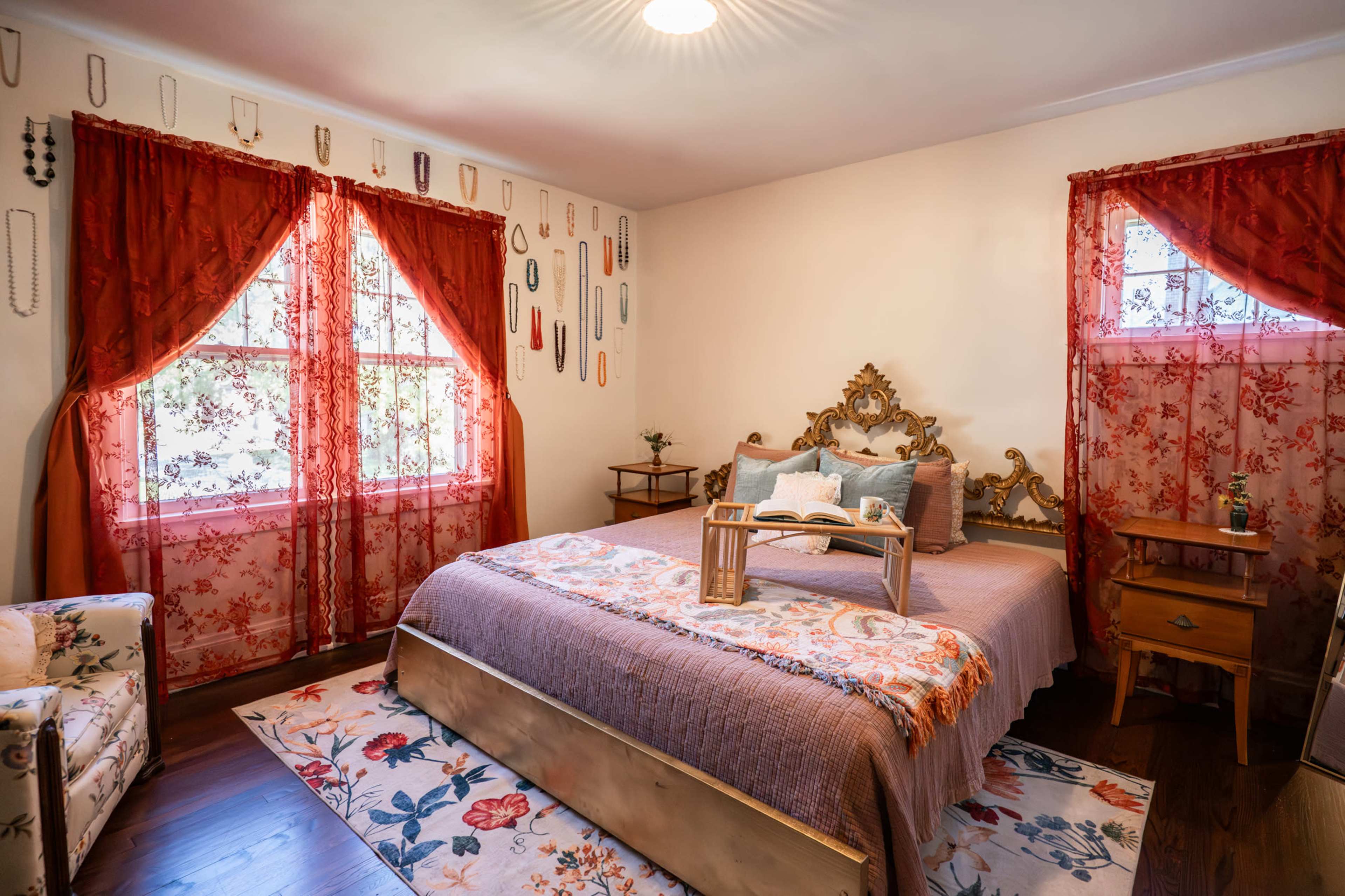 The room features a bed with a decorative headboard, surrounded by floral-patterned curtains and a matching area rug.