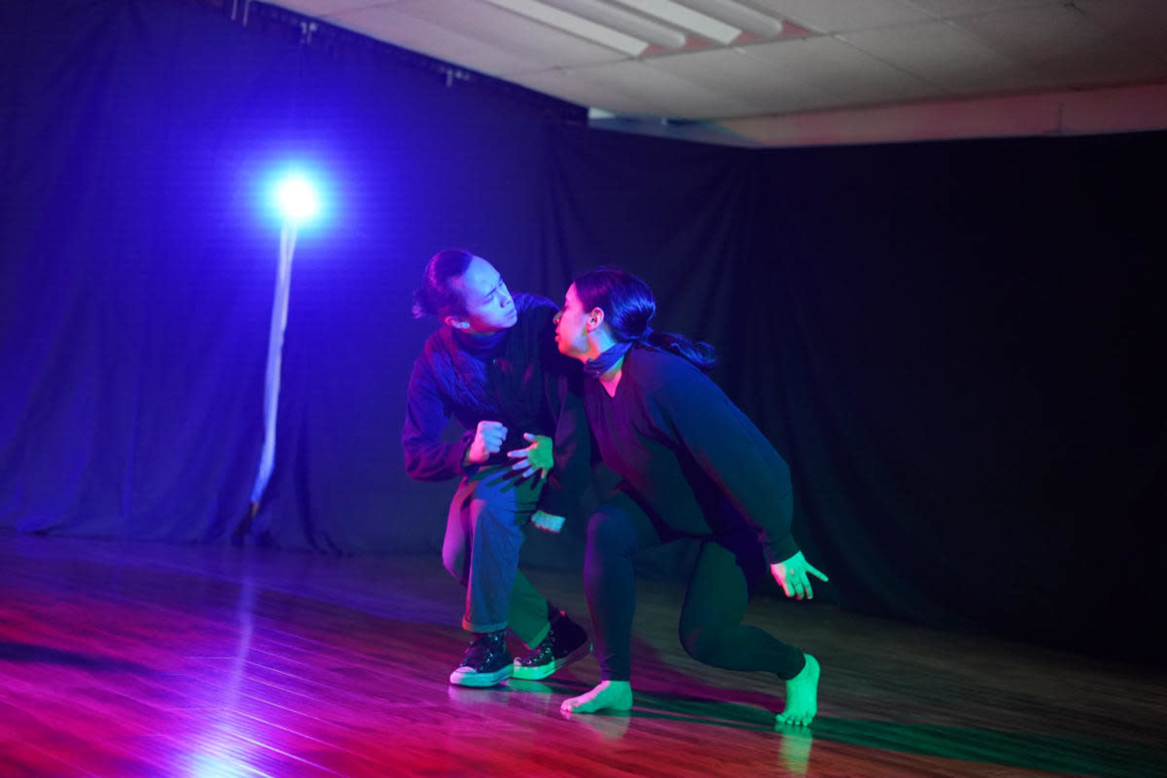 Two dancers perform in a dimly lit room with a spotlight casting colorful lights on them.