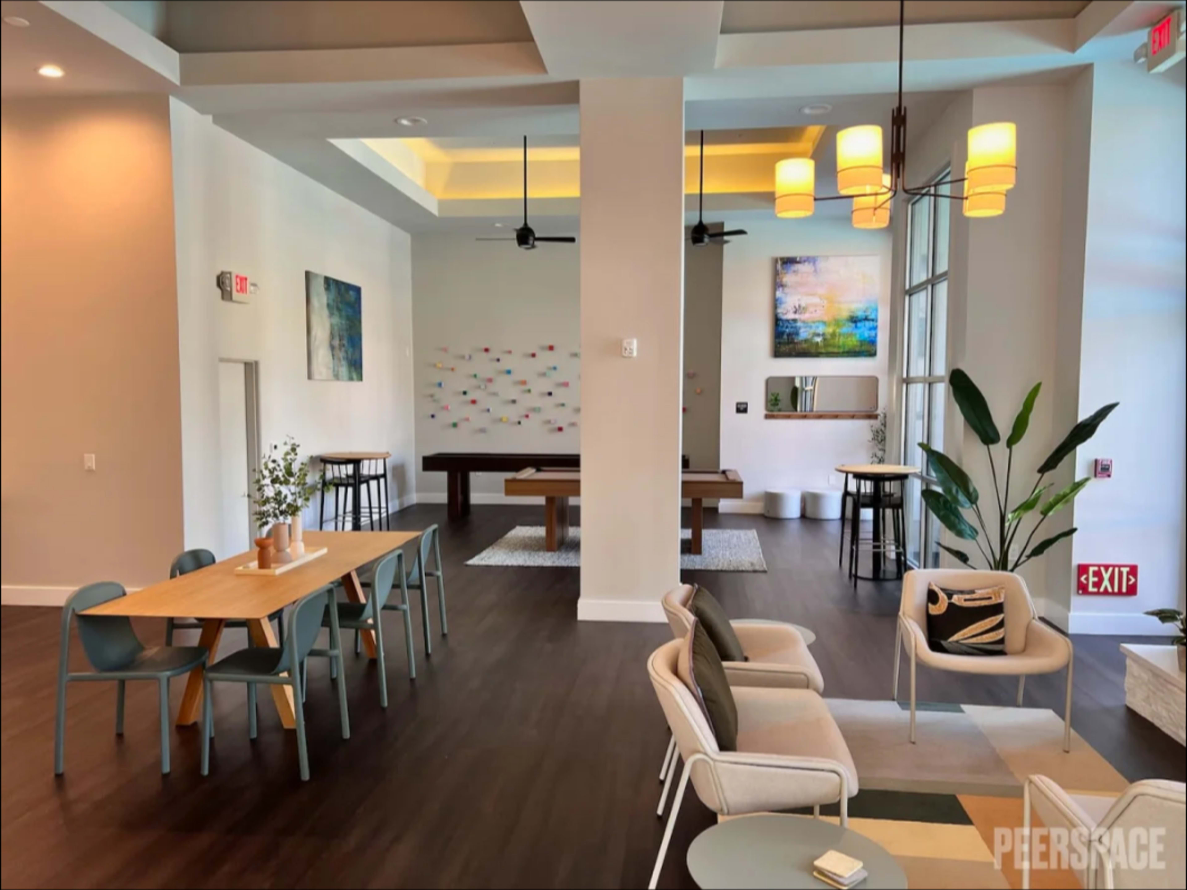 The image shows a modern interior space with seating areas, dining tables, and a billiard table, highlighted by large windows and vibrant wall art.