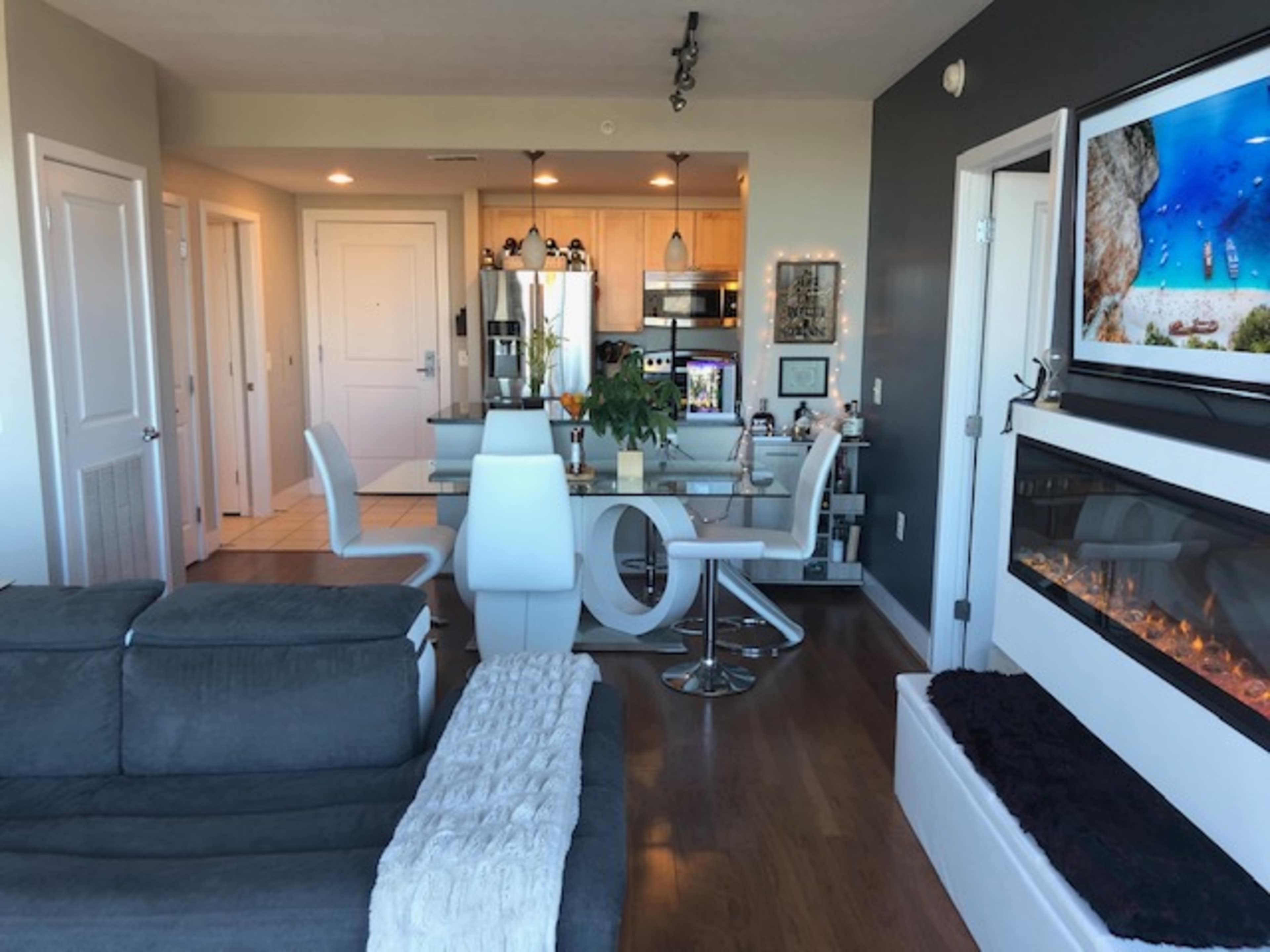 A modern living area and kitchen with a dining table, sleek furniture, and a wall-mounted fireplace.