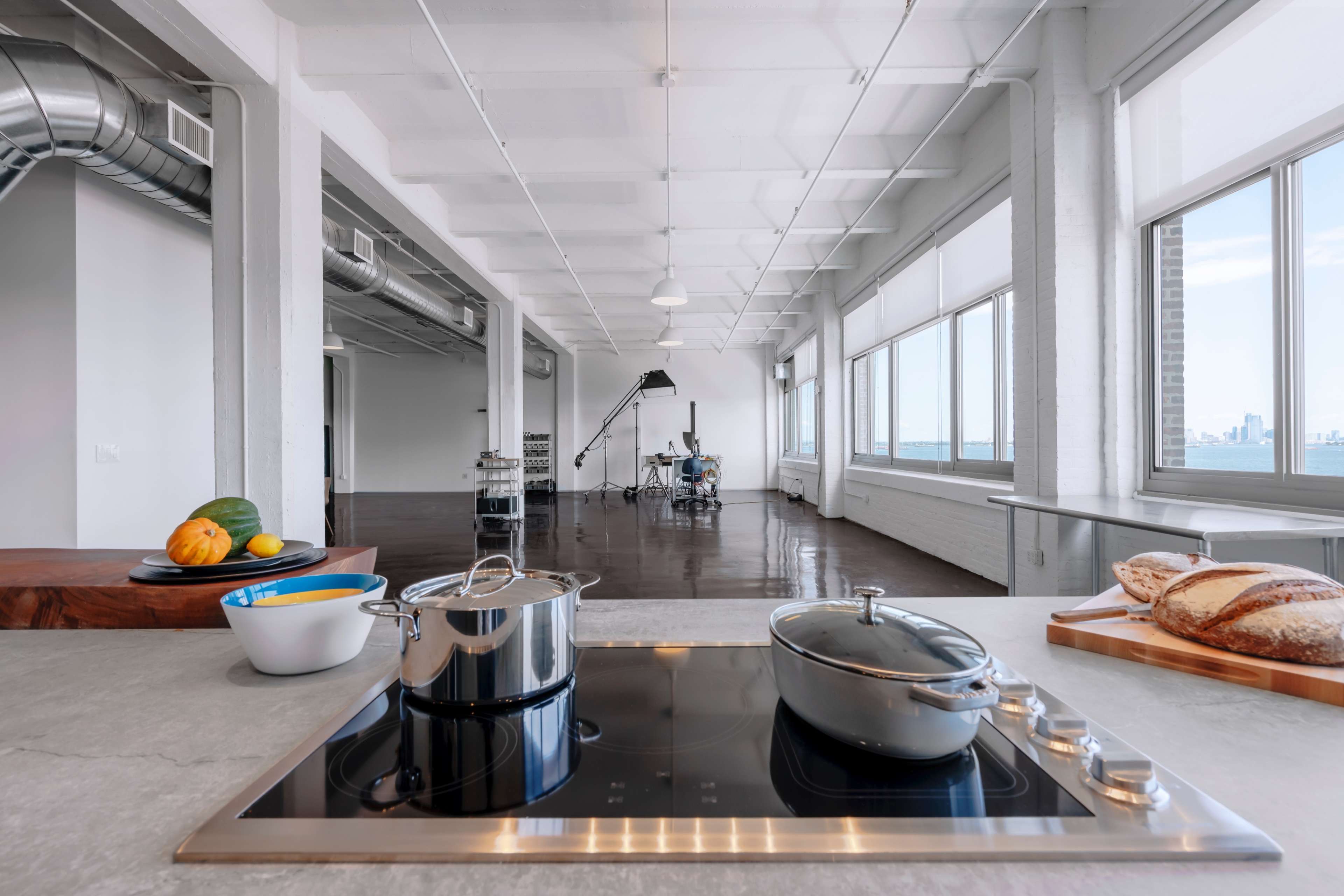 A modern kitchen features pots on a countertop overlooking a spacious, minimalist open-concept living area with large windows.