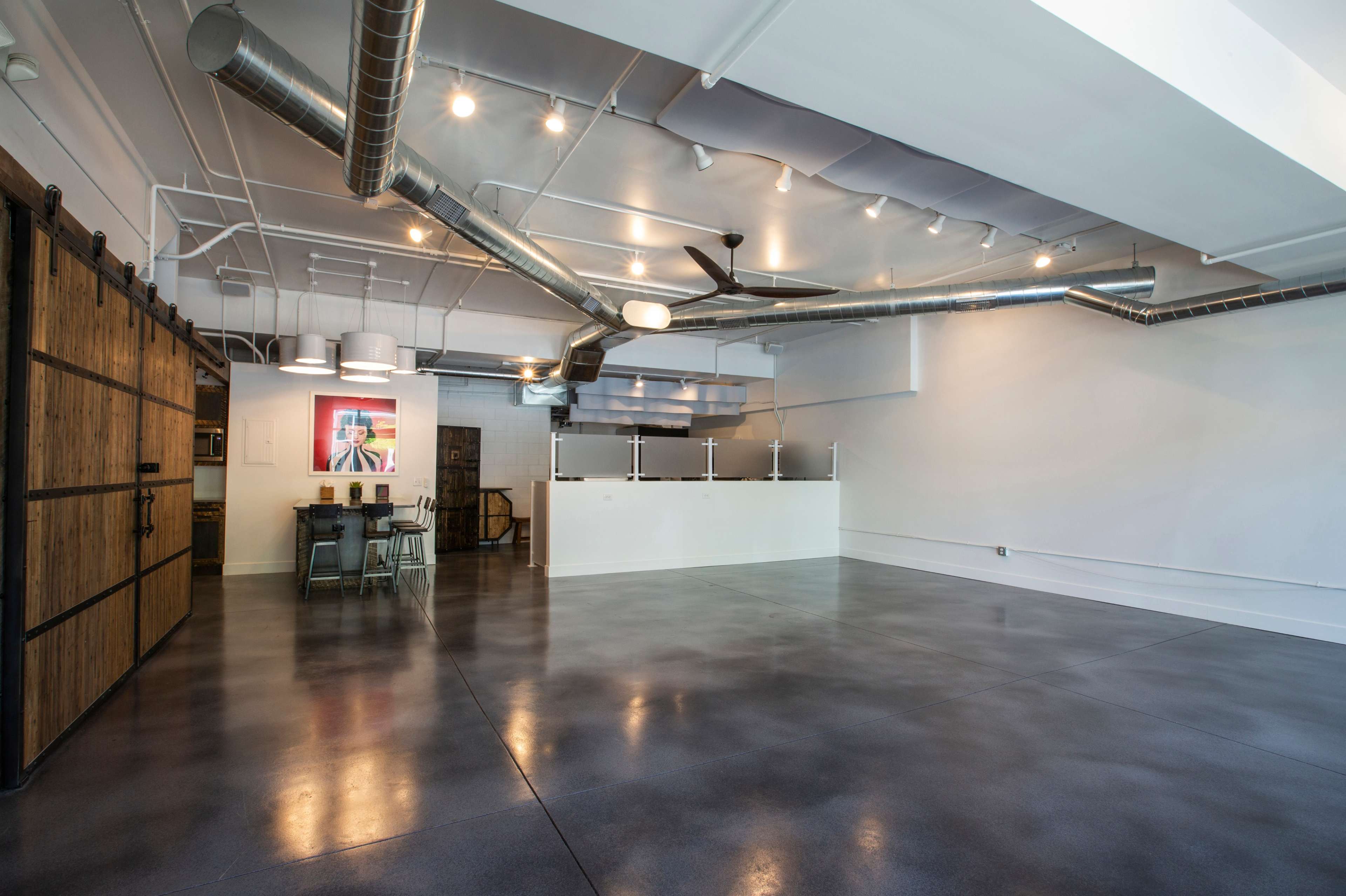 An open, modern interior space with polished concrete floors, exposed ductwork, and a large sliding wooden door.