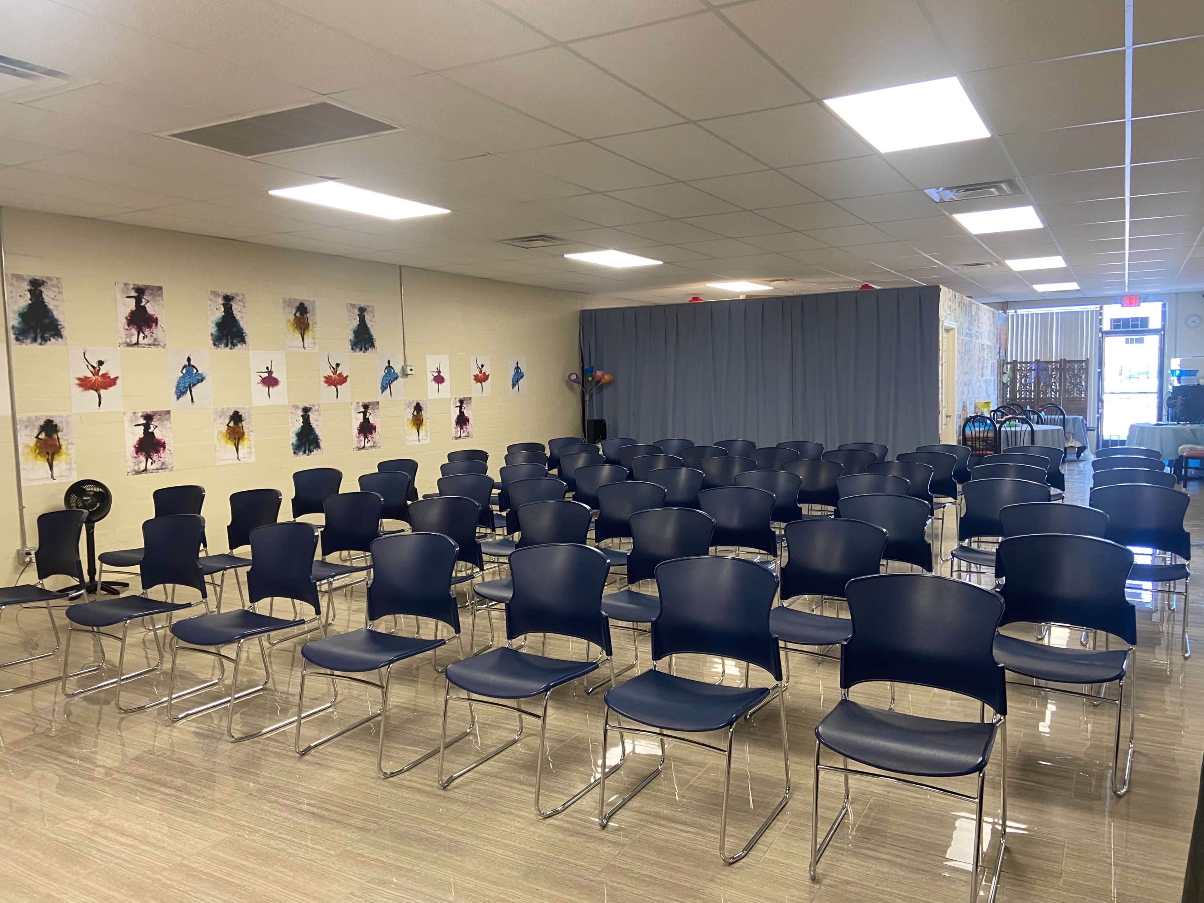 A rows of navy blue plastic chairs arranged in a large, well-lit room with artwork displayed on the walls.