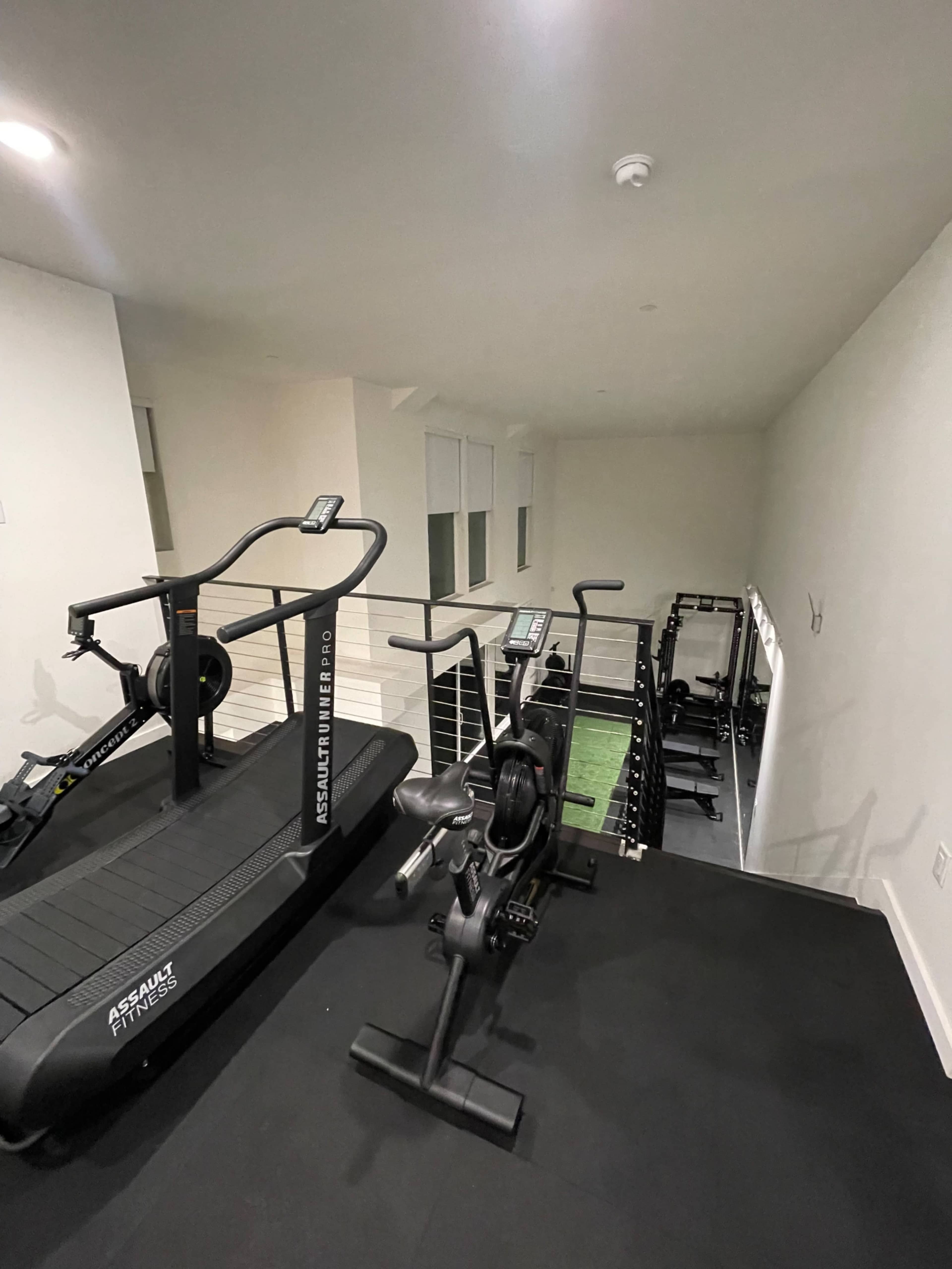 A modern home gym with various exercise equipment, including a treadmill and stationary bike, arranged on a black rubber floor.