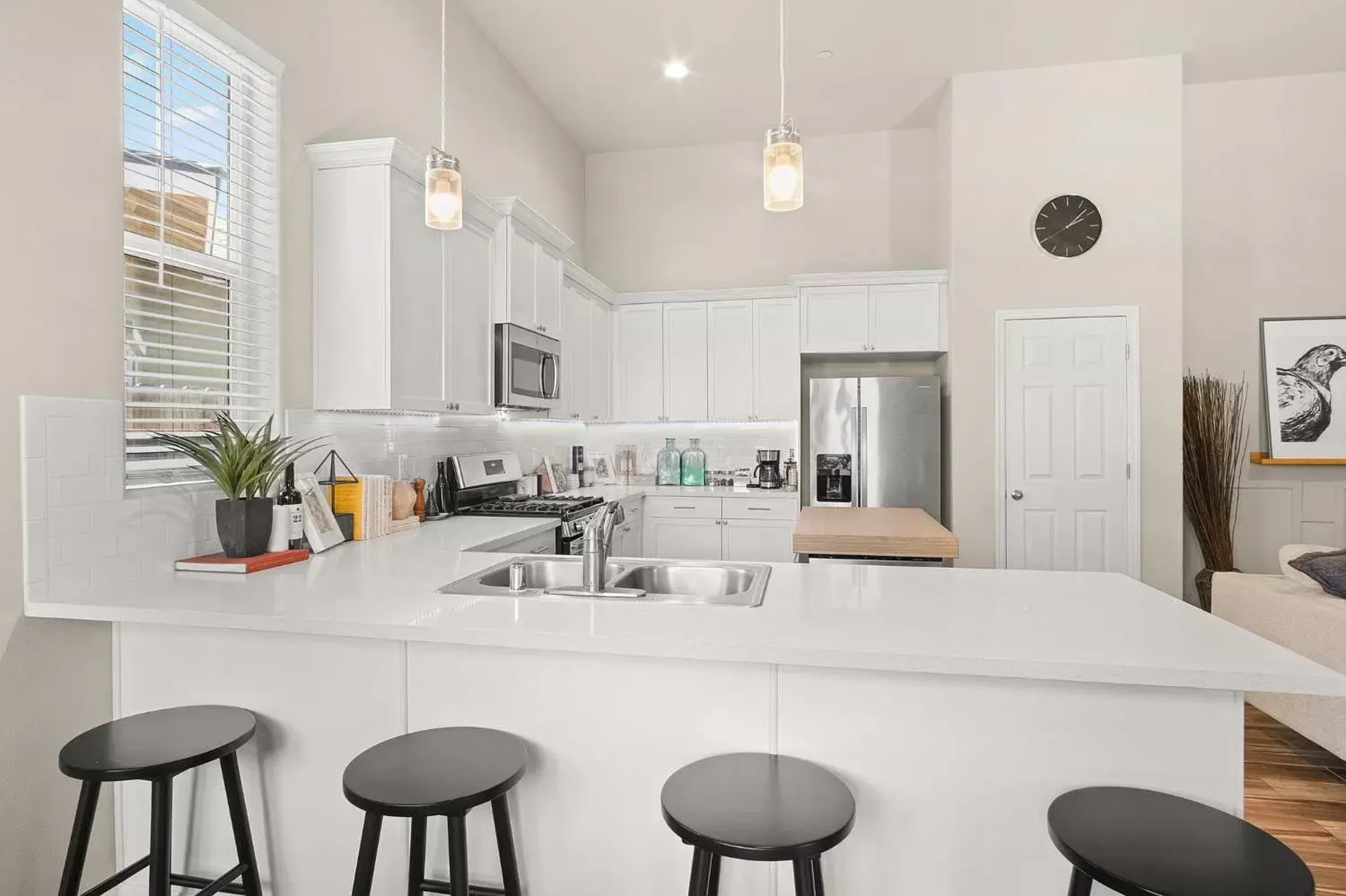 A modern kitchen with white cabinetry, a large island with bar stools, and stainless steel appliances.