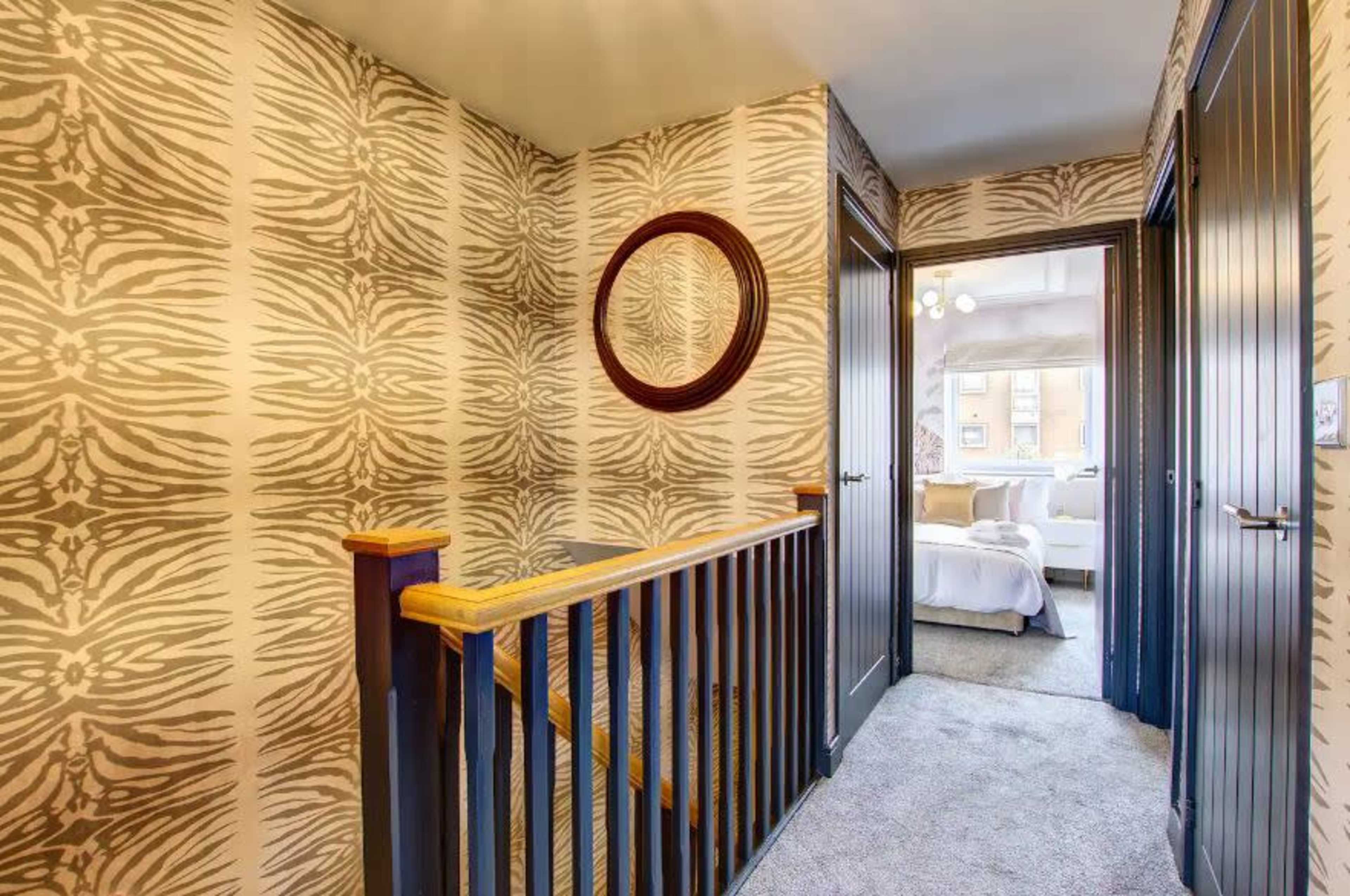 The image shows a hallway with zebra-striped wallpaper, a round mirror, and two dark doors leading to adjacent rooms.