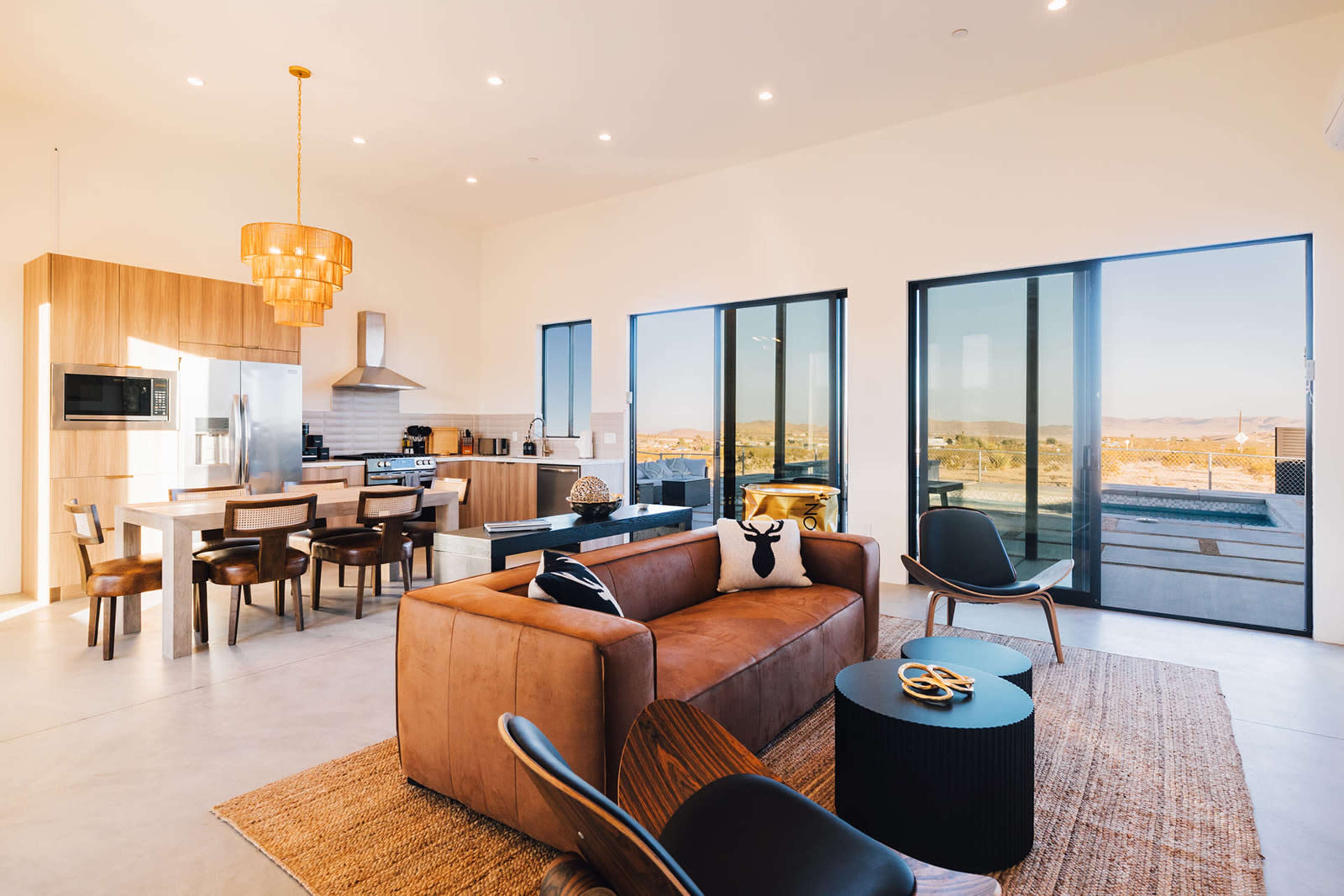 A modern open-concept living space featuring a kitchen, dining area, and living room with large windows offering a view of the outdoors.